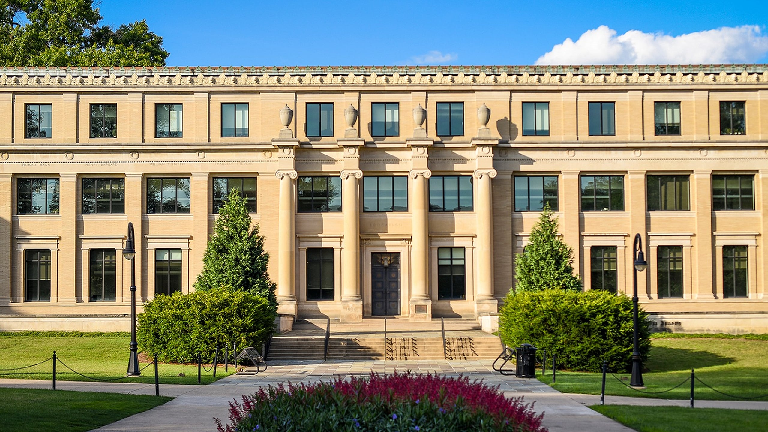 Grand Neoclassical building with impressive columns and lush landscaping on a bright sunny day.