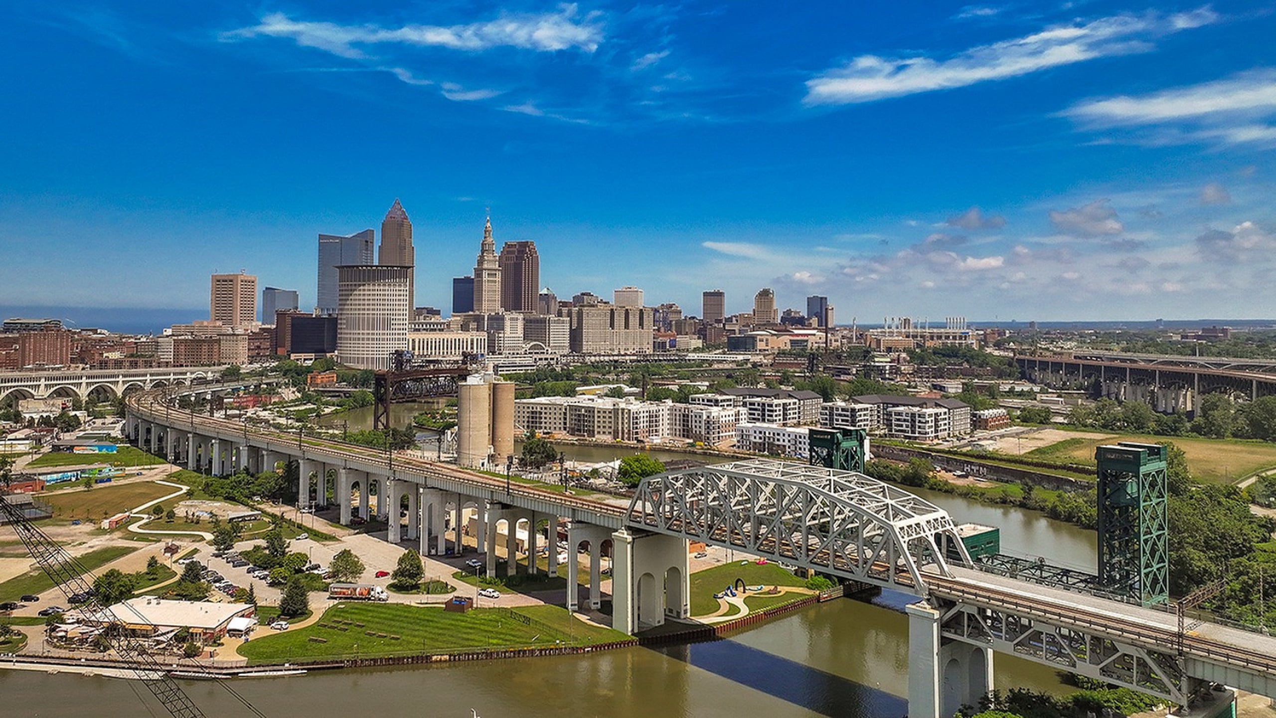 Breathtaking aerial view of a vibrant cityscape with modern skyscrapers, a winding river, and lush green spaces, all under a clear blue sky.