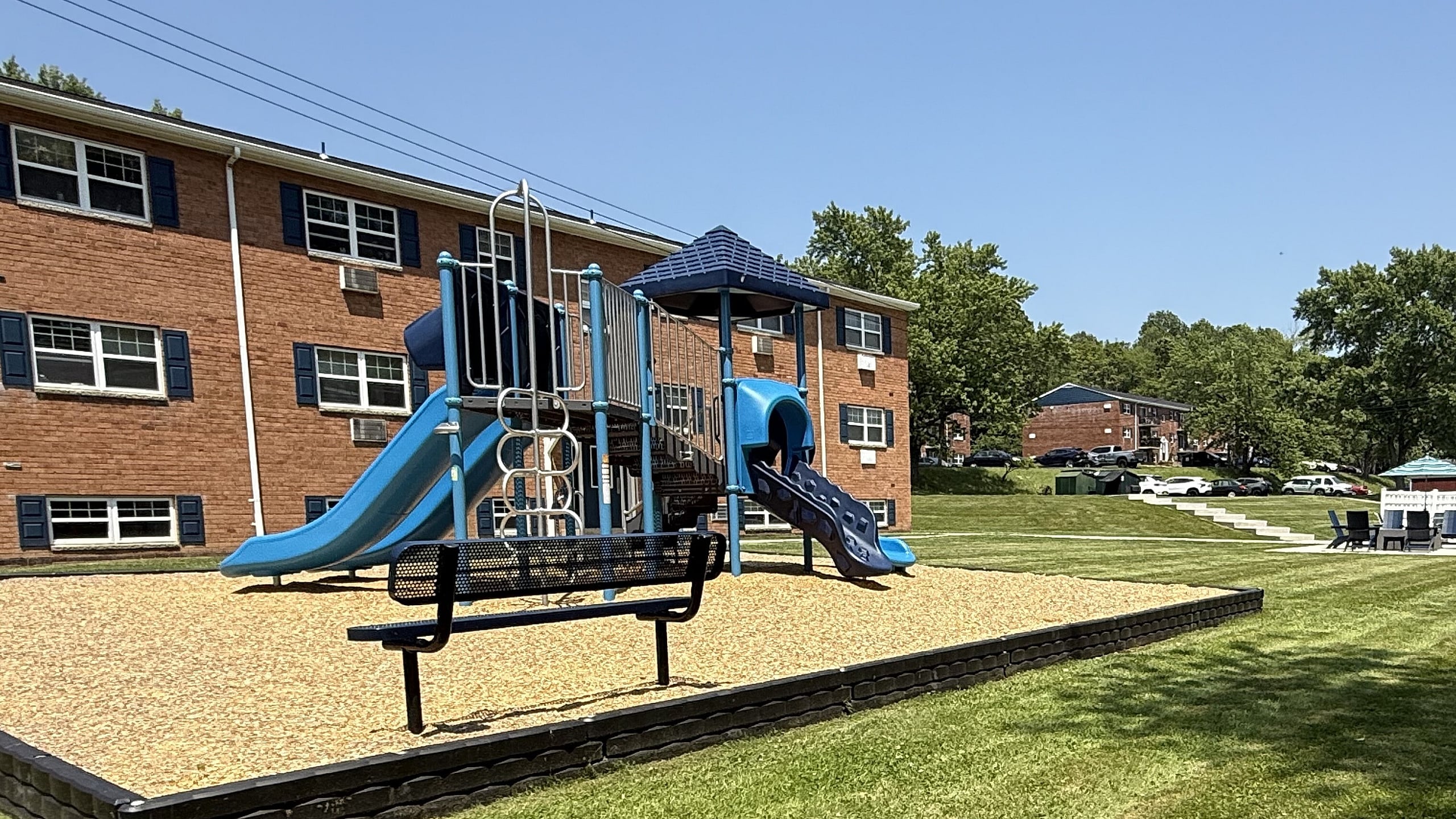 Charming apartment playground with vibrant blue slides, situated in a lush green lawn setting, perfect for family living.