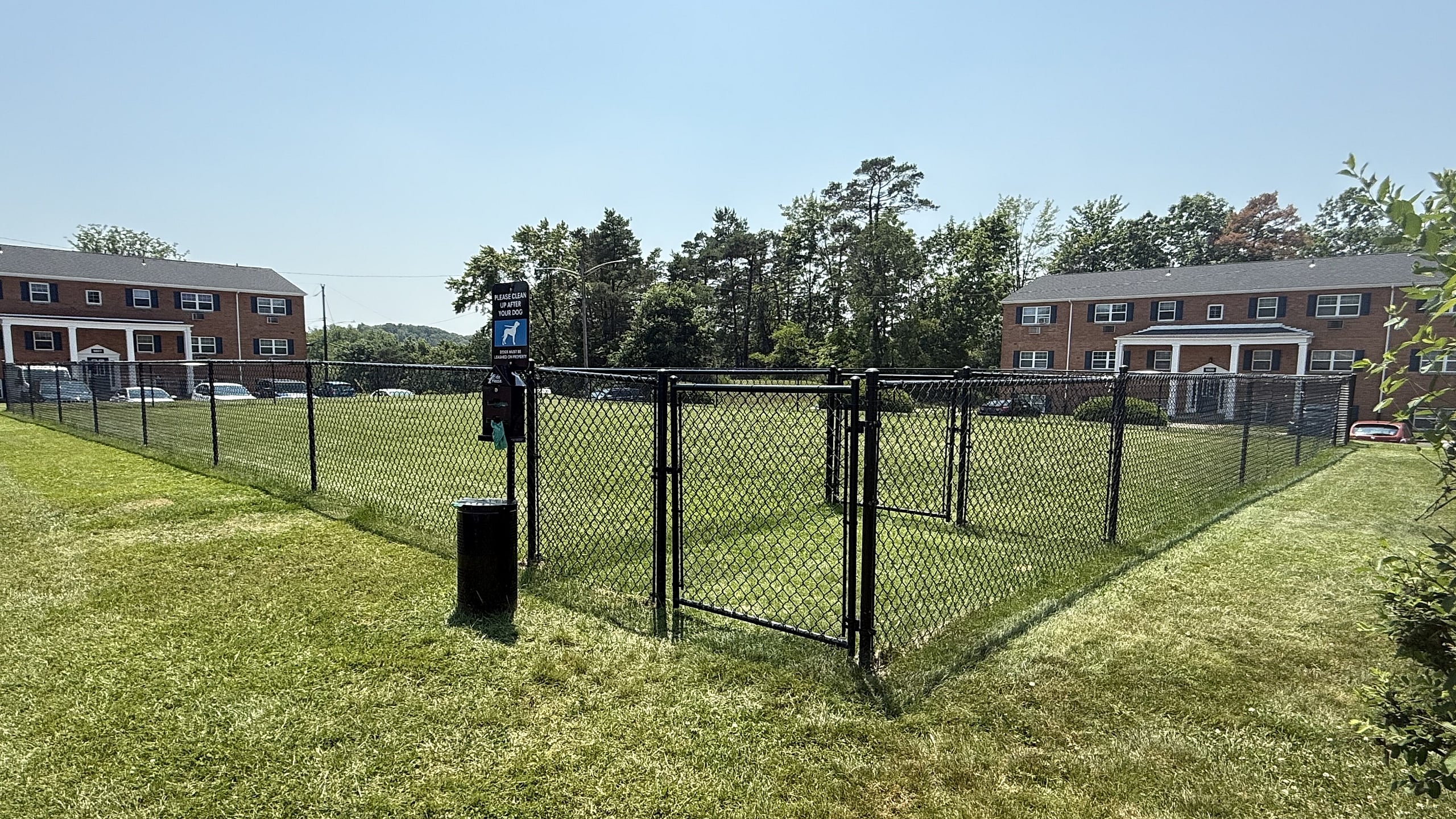 Charming community view with brick buildings and a lush fenced dog park, perfect for pet lovers.