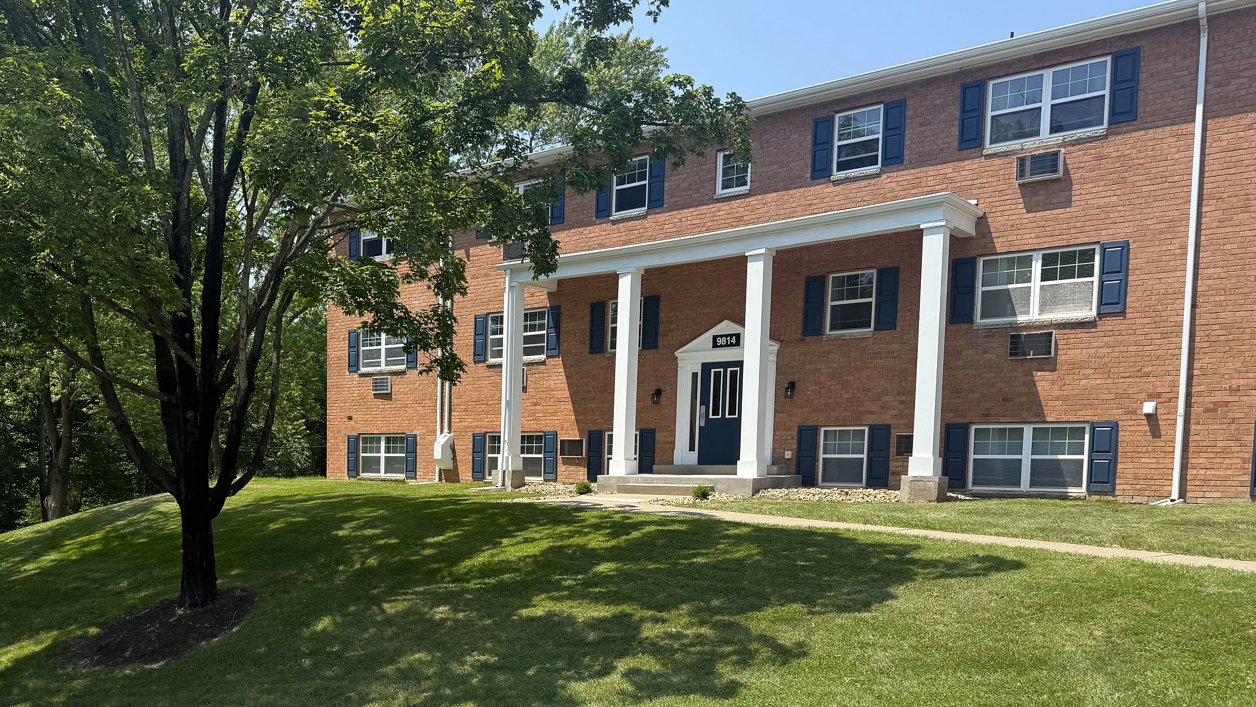 Charming brick apartment building with lush green lawn and inviting entrance, perfect for serene living.