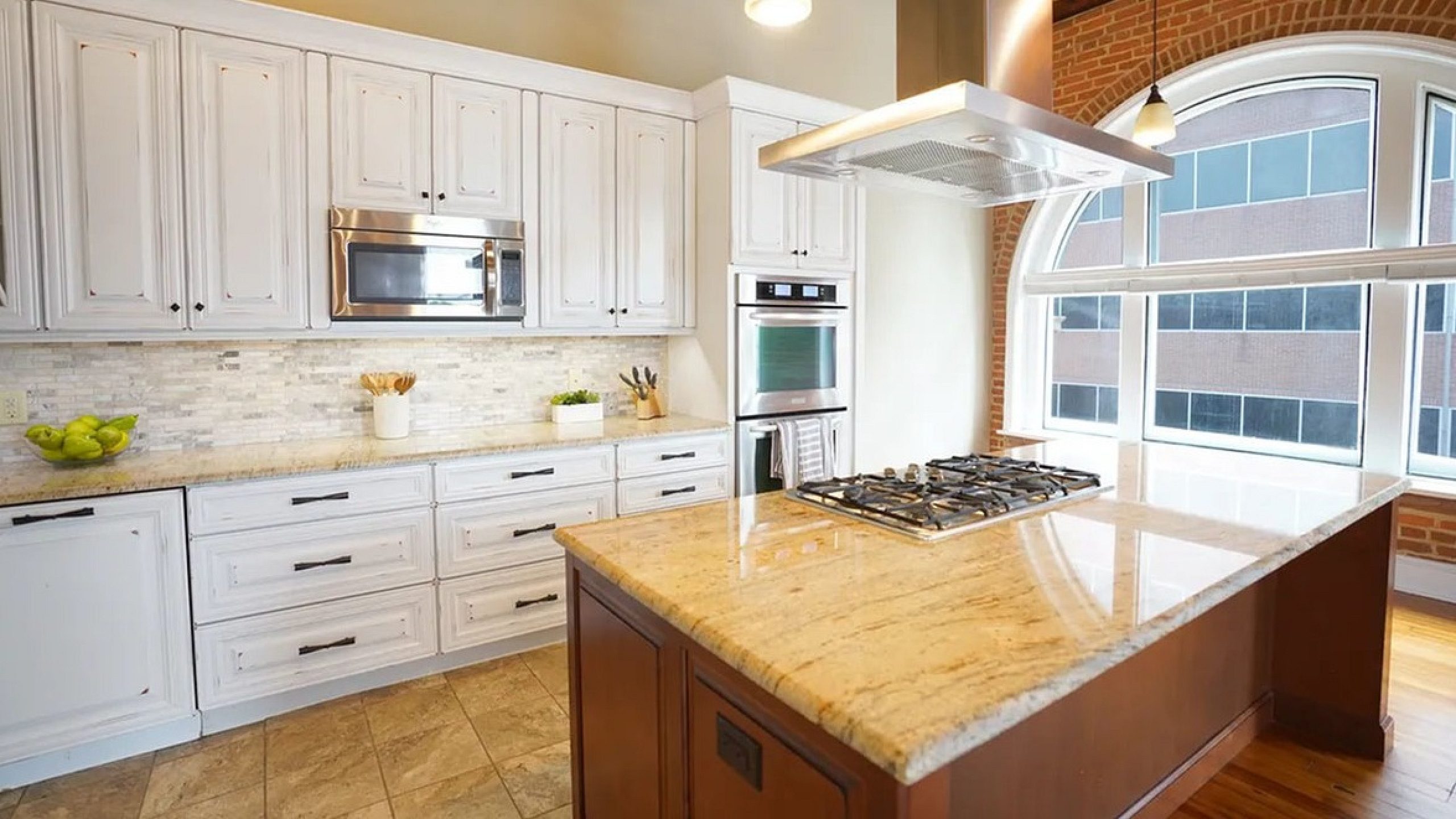 Elegant kitchen with large granite island, modern appliances, and abundant natural light from arched windows.