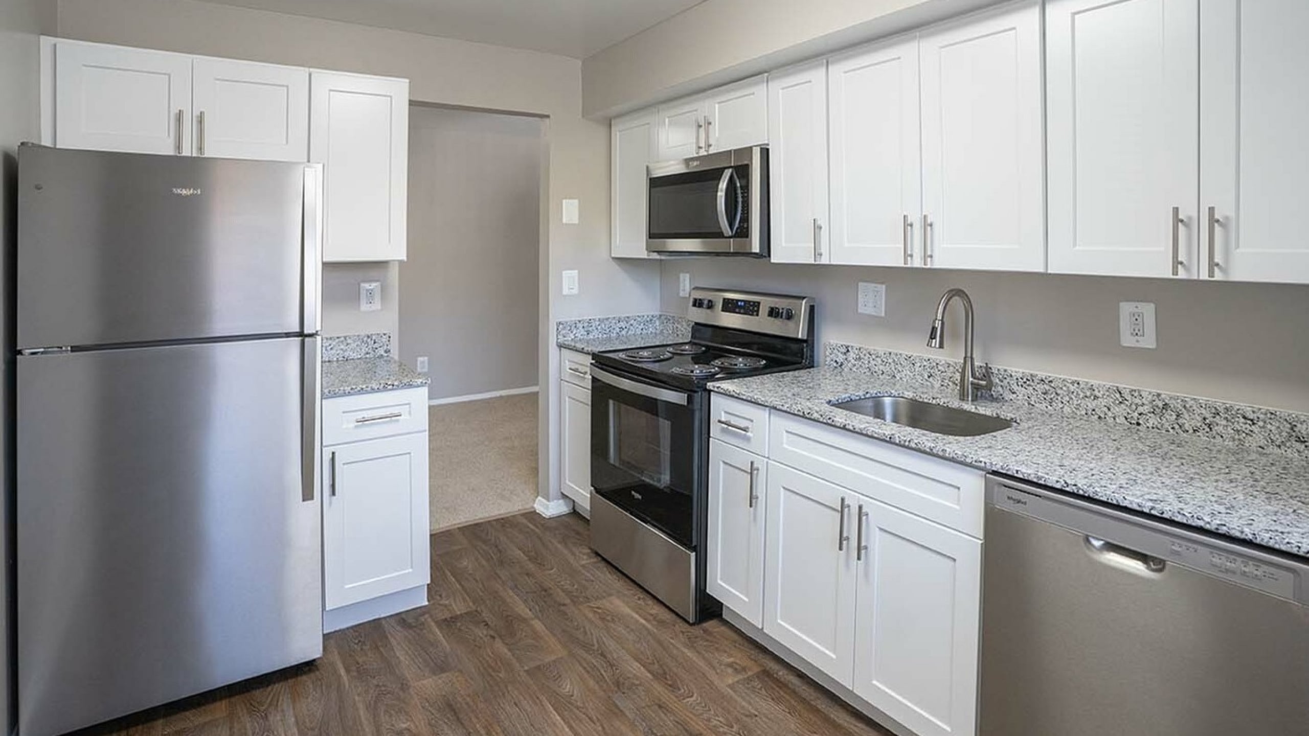 Modern kitchen showcasing sleek stainless steel appliances, elegant granite countertops, and stylish white cabinetry with a contemporary wood floor finish.