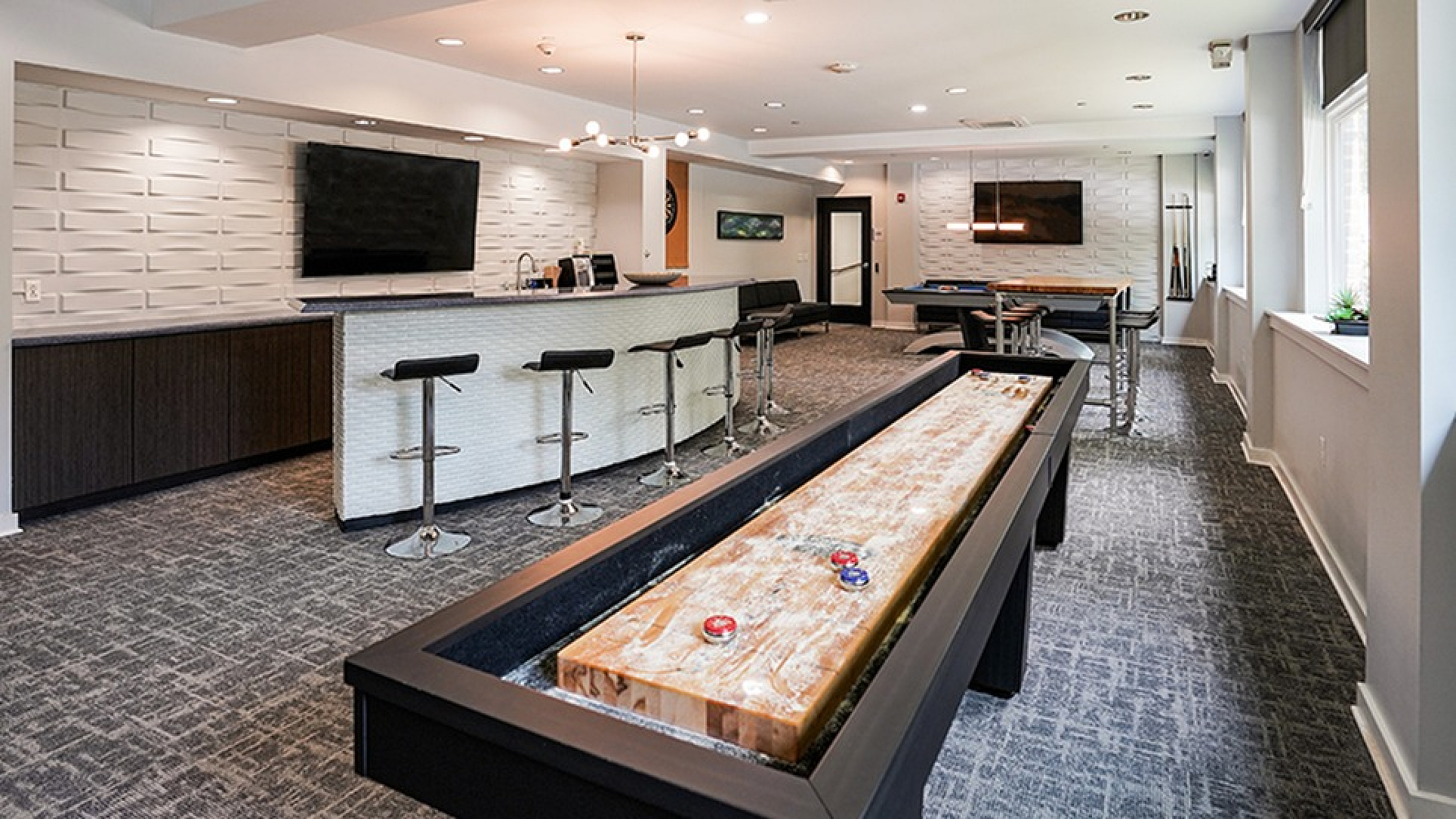 Chic apartment lounge featuring a sleek bar area, modern seating, and an entertaining shuffleboard setup.