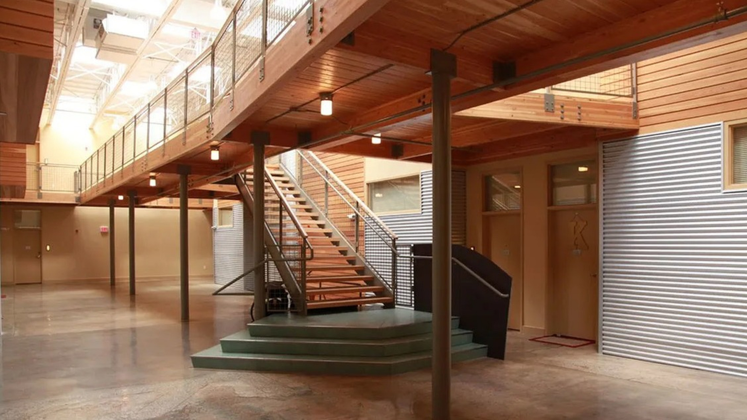 Modern, inviting apartment complex with open-industrial design, featuring exposed beams, stylish lighting, and a sleek metal staircase.