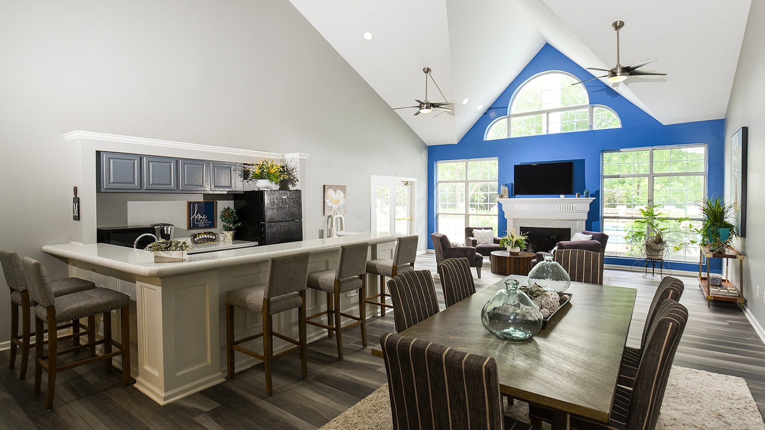 Bright and modern living space with vaulted ceilings, open kitchen with breakfast bar, and airy dining area, featuring large windows and vibrant interior.