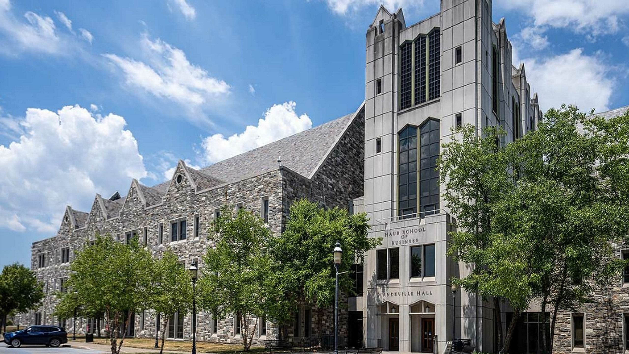 Elegant stone building with Gothic architecture surrounded by lush trees under a vibrant blue sky.