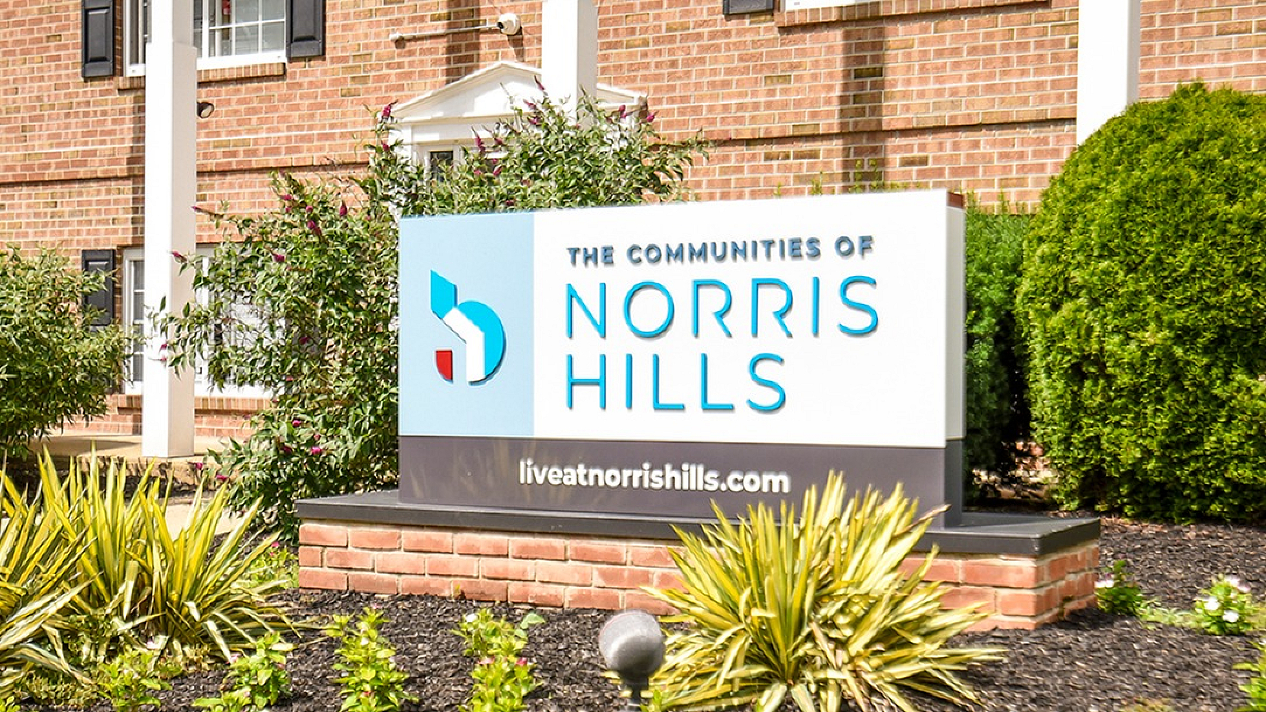 Inviting entrance of The Communities of Norris Hills with lush greenery and bold signage.