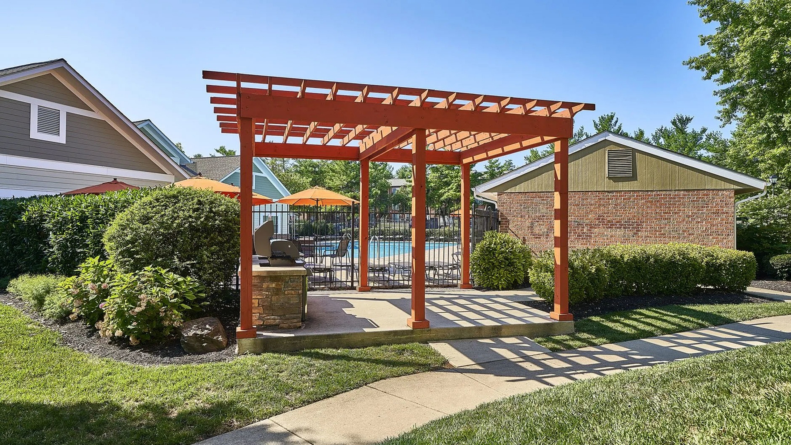 Charming outdoor patio with pergola and modern grill, set against a backdrop of lush greenery and vibrant poolside ambiance.