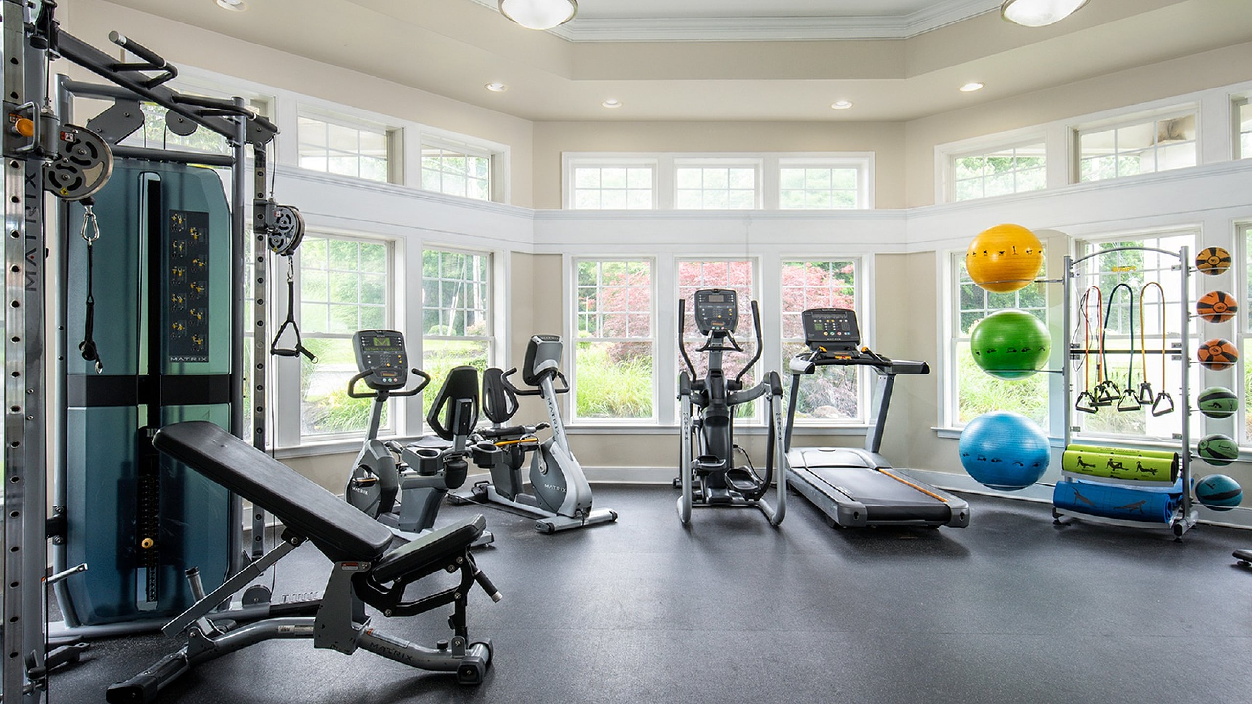 Bright and spacious home gym featuring modern exercise equipment, large windows providing natural light, and vibrant fitness accessories.