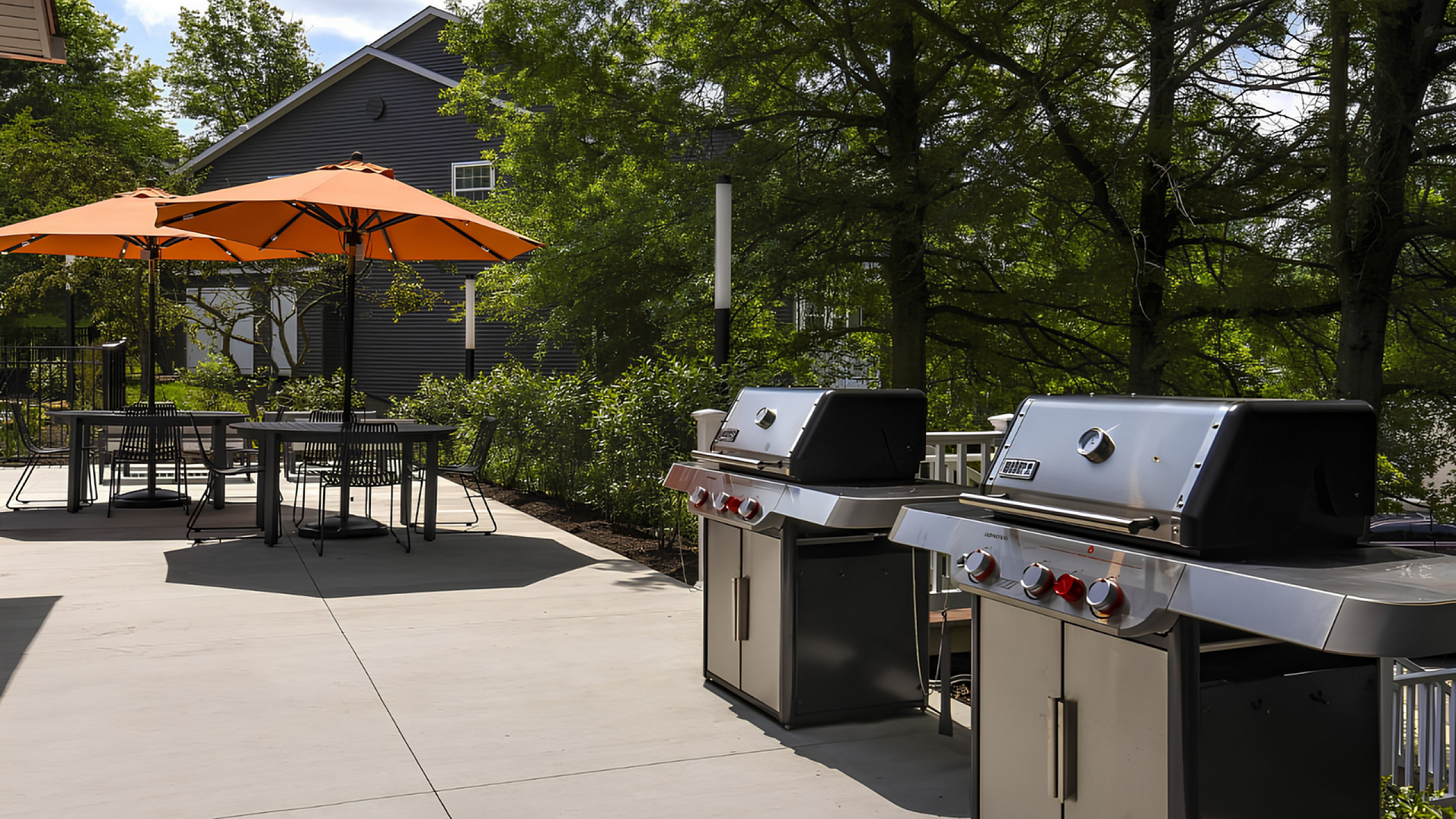Charming outdoor patio with modern grills, vibrant orange umbrellas, and lush greenery for peaceful gatherings.