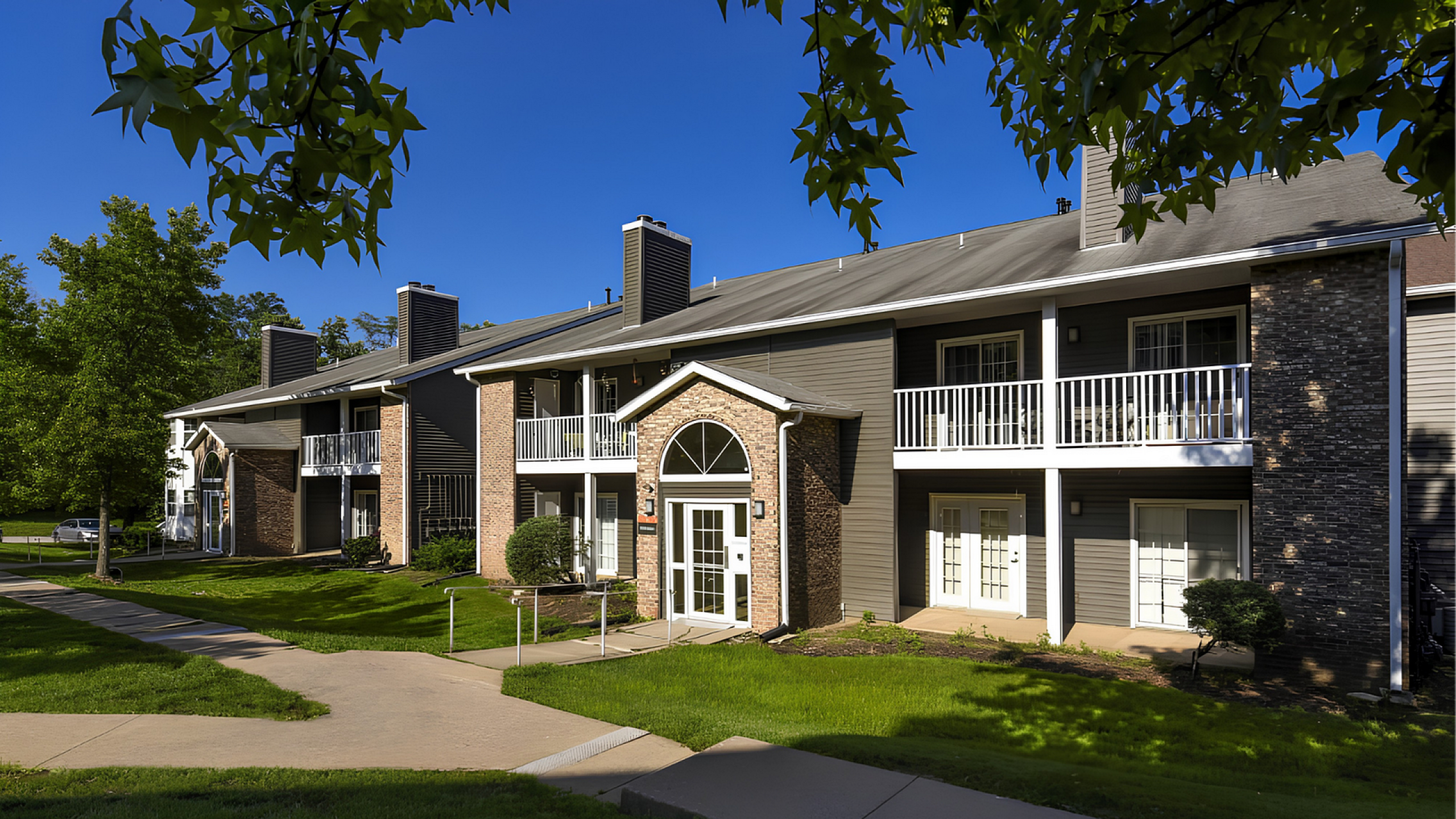 Charming apartment complex with modern design, featuring spacious balconies, lush green surroundings, and elegant brick facade.