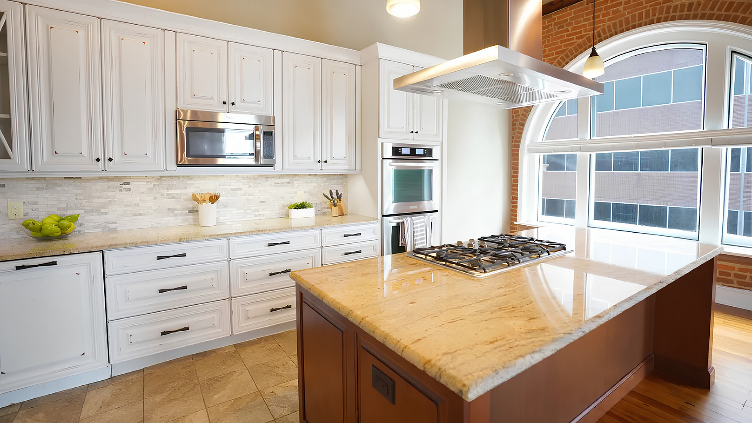 Elegant kitchen with bright white cabinetry, modern stainless steel appliances, and a spacious granite island under a sleek range hood, bathed in natural light from large arched windows.