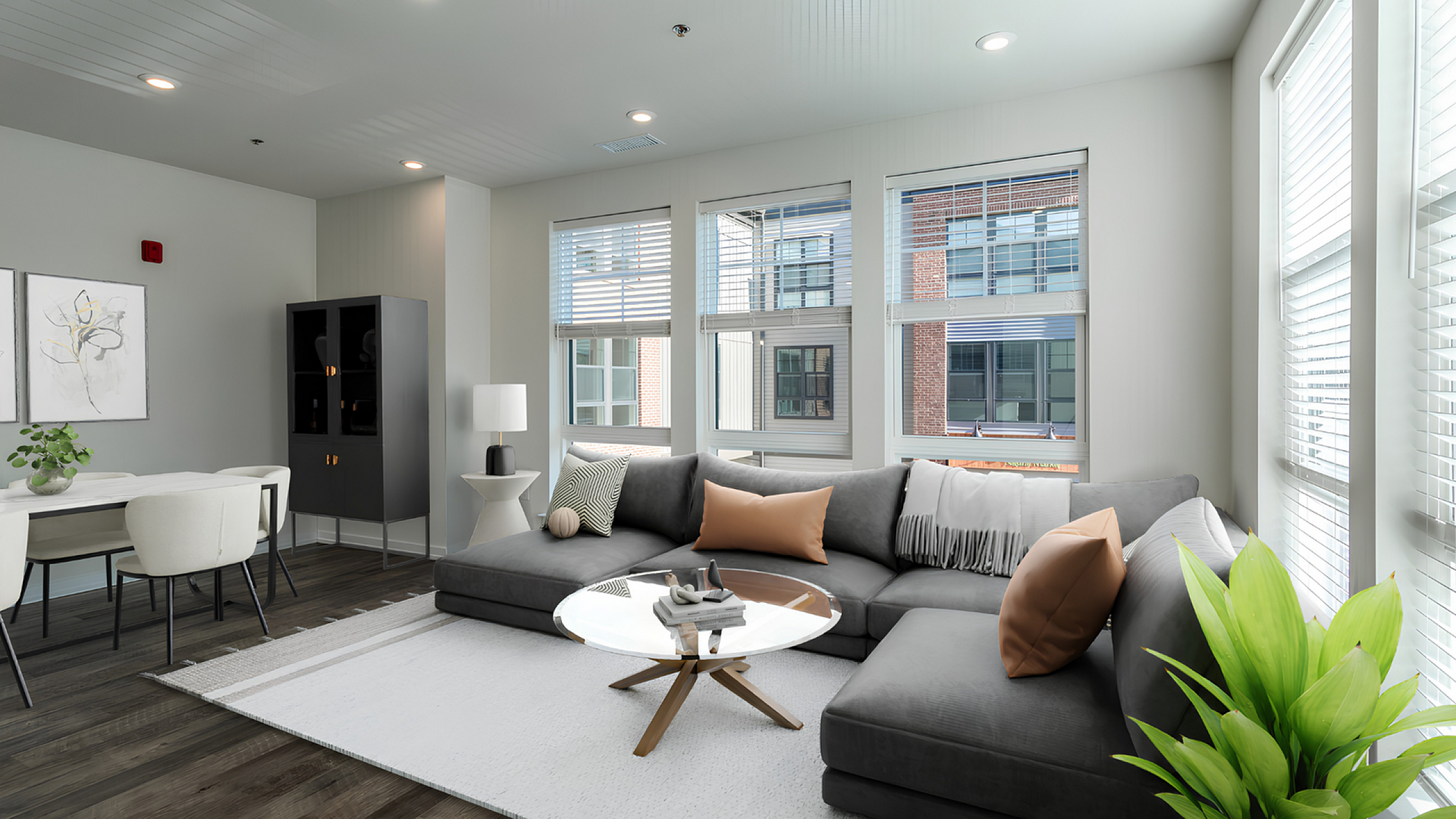 Bright and stylish living room with a modern gray sectional sofa, chic glass coffee table, and large windows providing plenty of natural light.