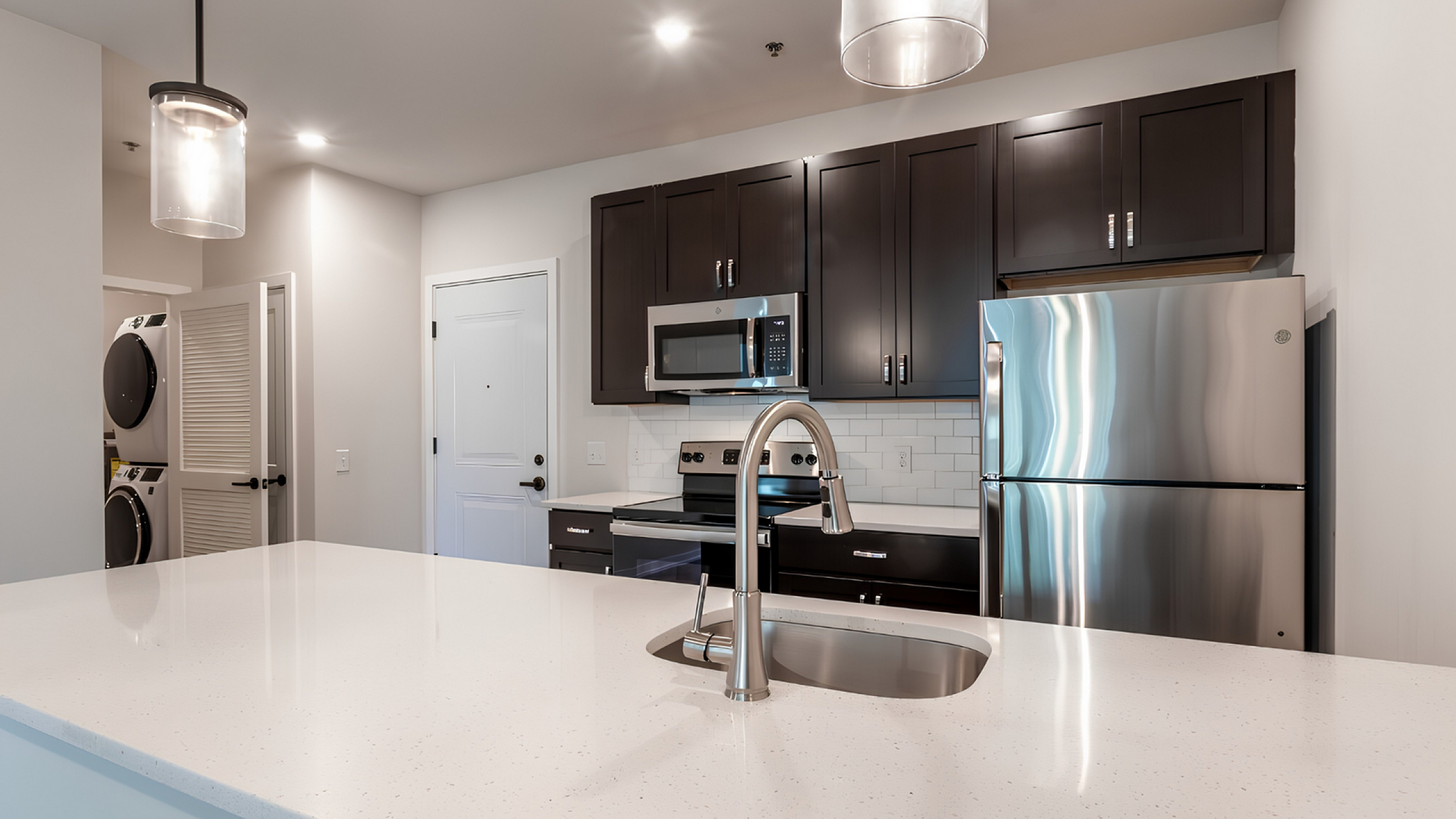 Sleek modern kitchen with stainless steel appliances, elegant dark cabinets, and a pristine white countertop, perfect for stylish living.