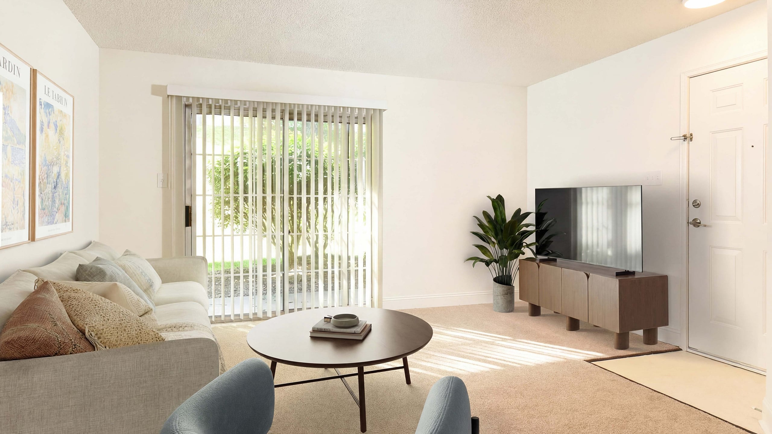 Bright and inviting living room with modern decor, sleek TV stand, plush seating, and natural light streaming through large windows with vertical blinds.