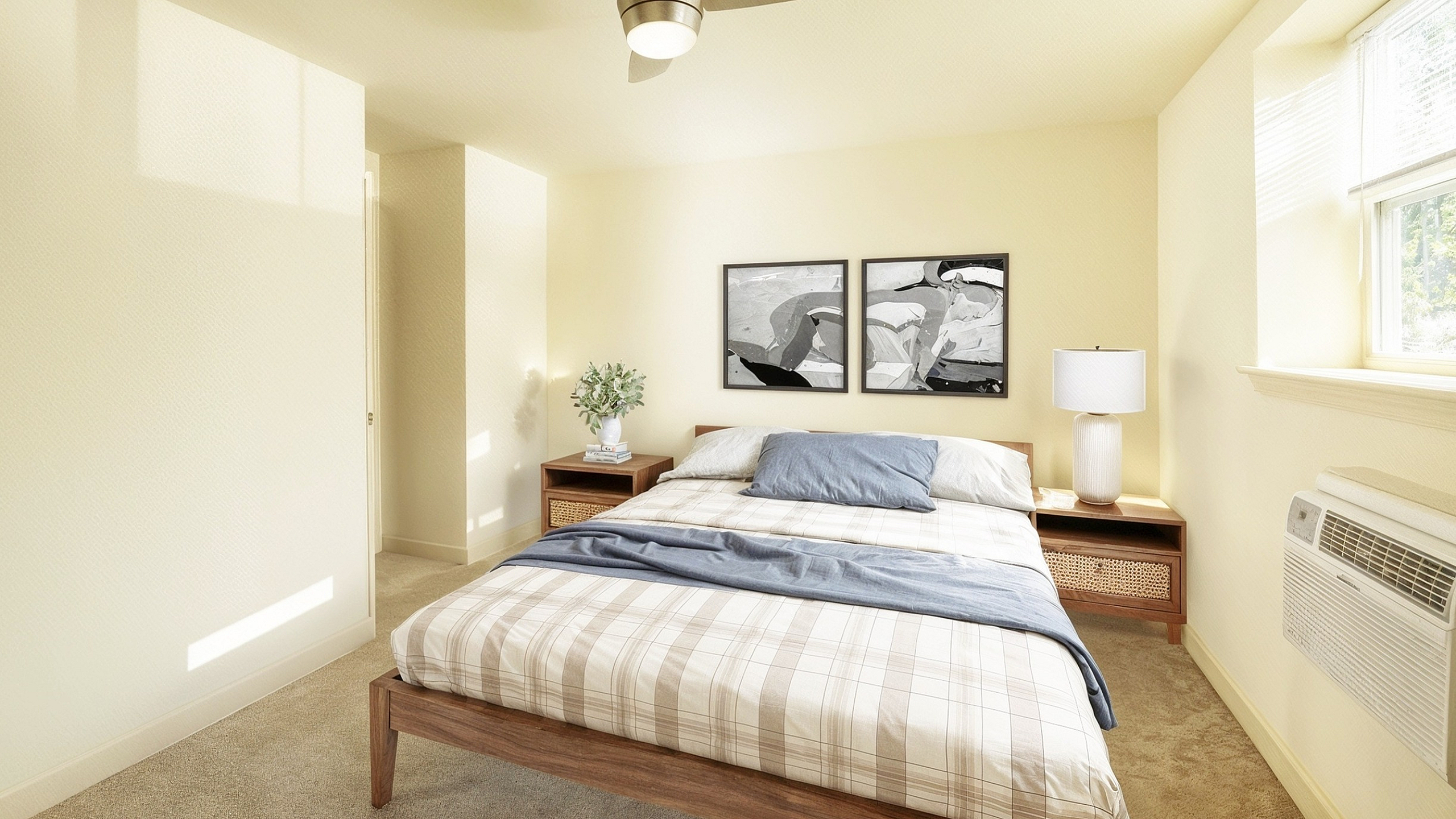 Inviting bedroom with warm beige tones, featuring a stylish ceiling fan, modern artwork, and large window for abundant natural light.