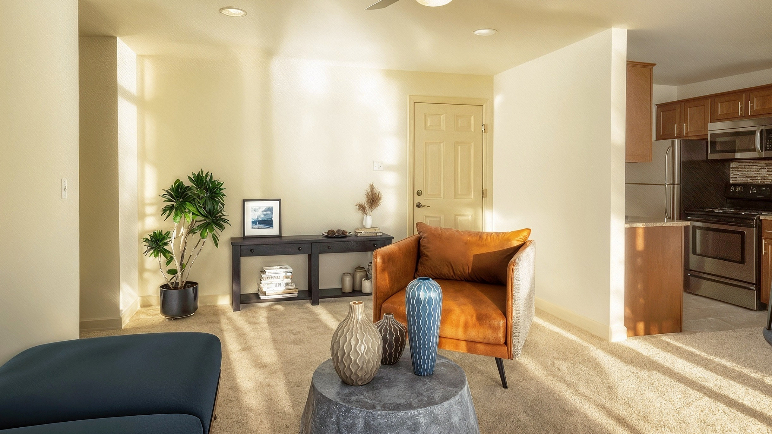 Bright and inviting living space with modern decor, featuring a cozy armchair, artistic vases, and an open-concept kitchen in the background.