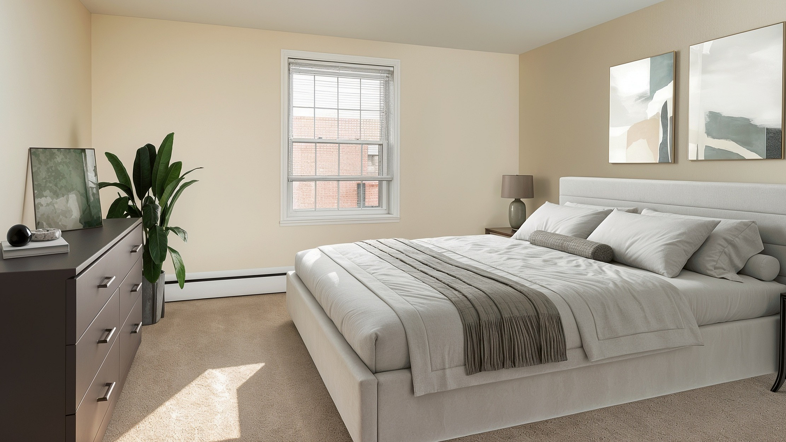 Bright and airy bedroom featuring a large bed with soft bedding, modern dresser, and contemporary artwork, complemented by natural sunlight and elegant indoor plant.