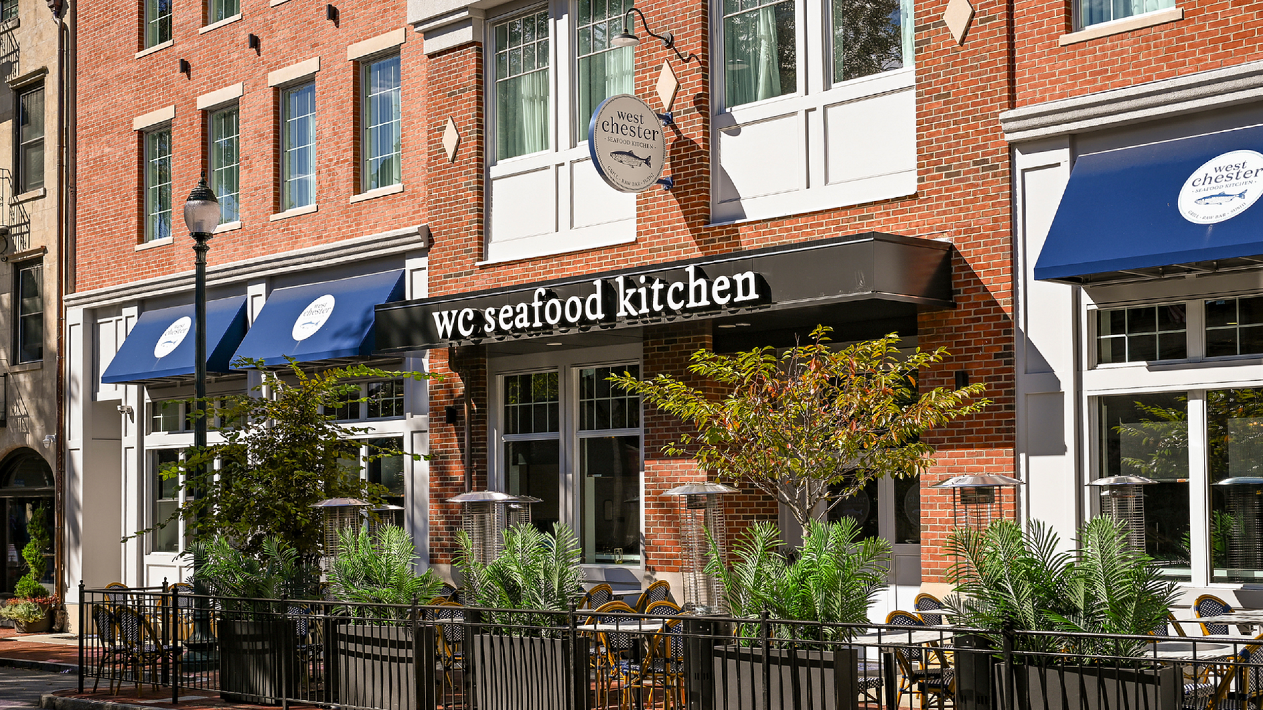 Charming brick facade of WC Seafood Kitchen adorned with stylish awnings and inviting outdoor seating, offering a vibrant dining experience.