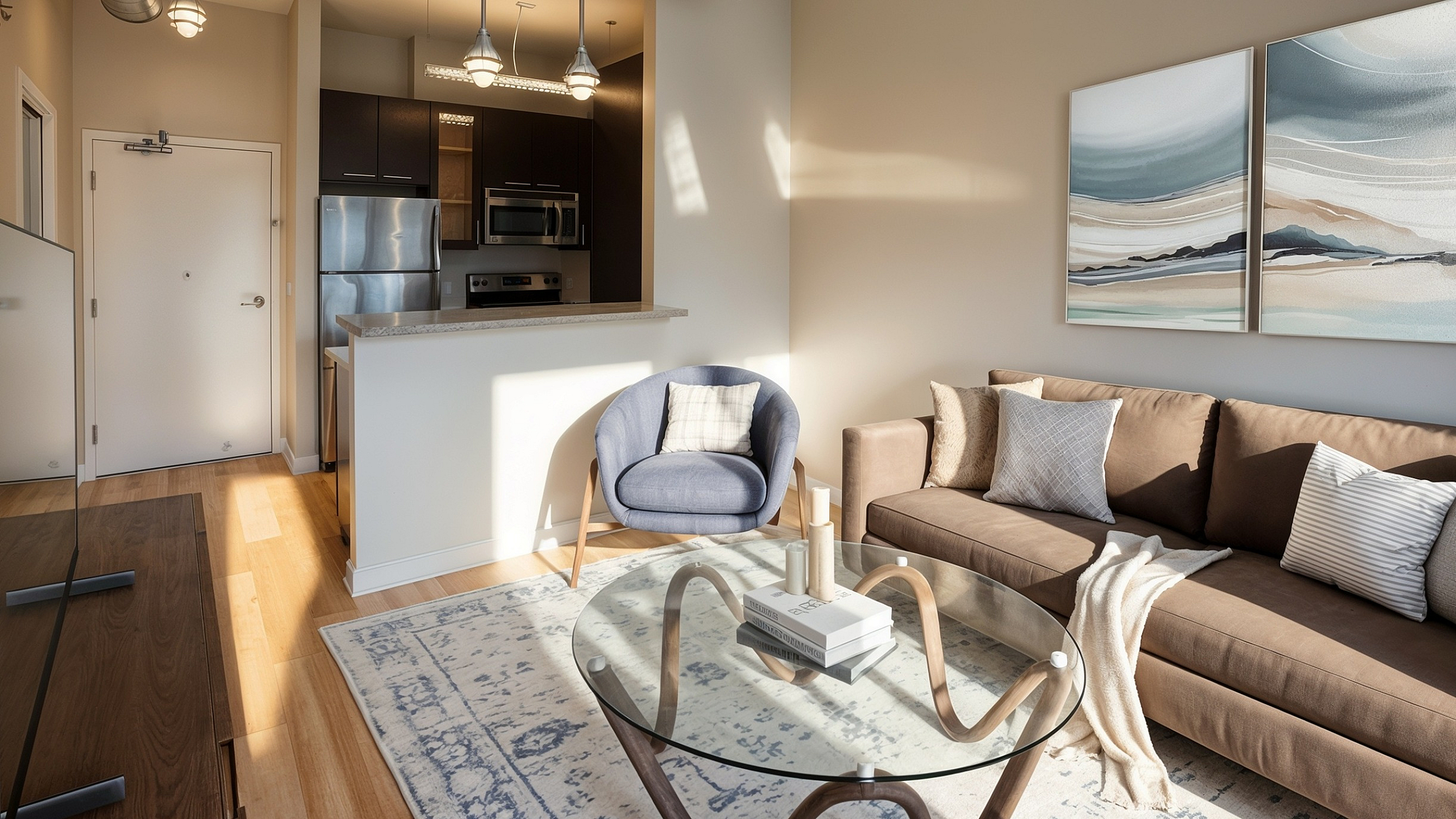 Bright and modern living room with stylish furniture, featuring a cozy sofa, chic glass coffee table, and contemporary art, leading into a sleek open kitchen with stainless steel appliances.