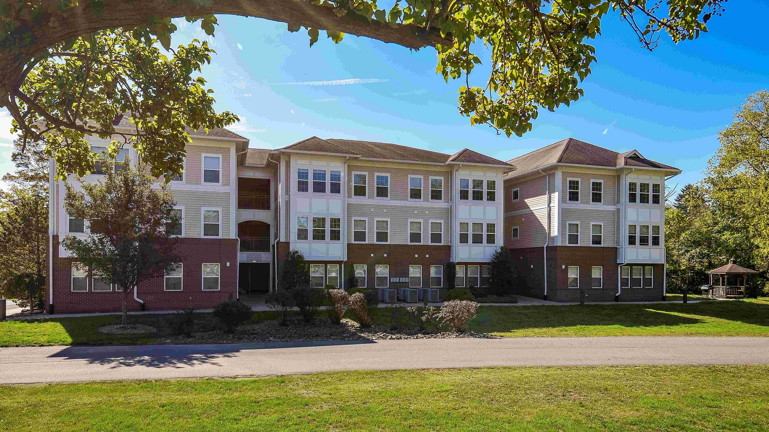Charming multi-story apartment building with elegant brick and siding facade, nestled in a lush, green landscape under a vibrant blue sky.