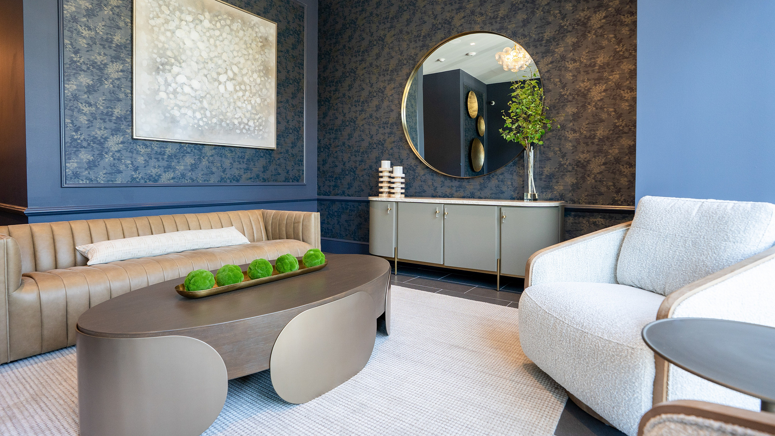 Chic living room with plush seating, modern art, and elegant decor set against textured blue walls.