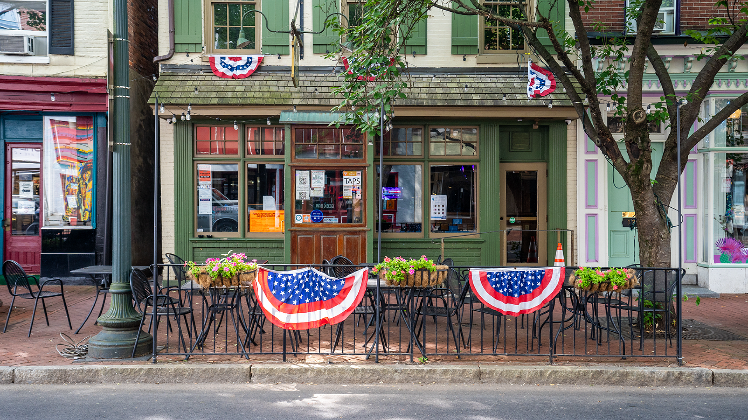 Charming caf&eacute; exterior with festive American flag decorations, outdoor seating, and inviting vintage-style architecture.