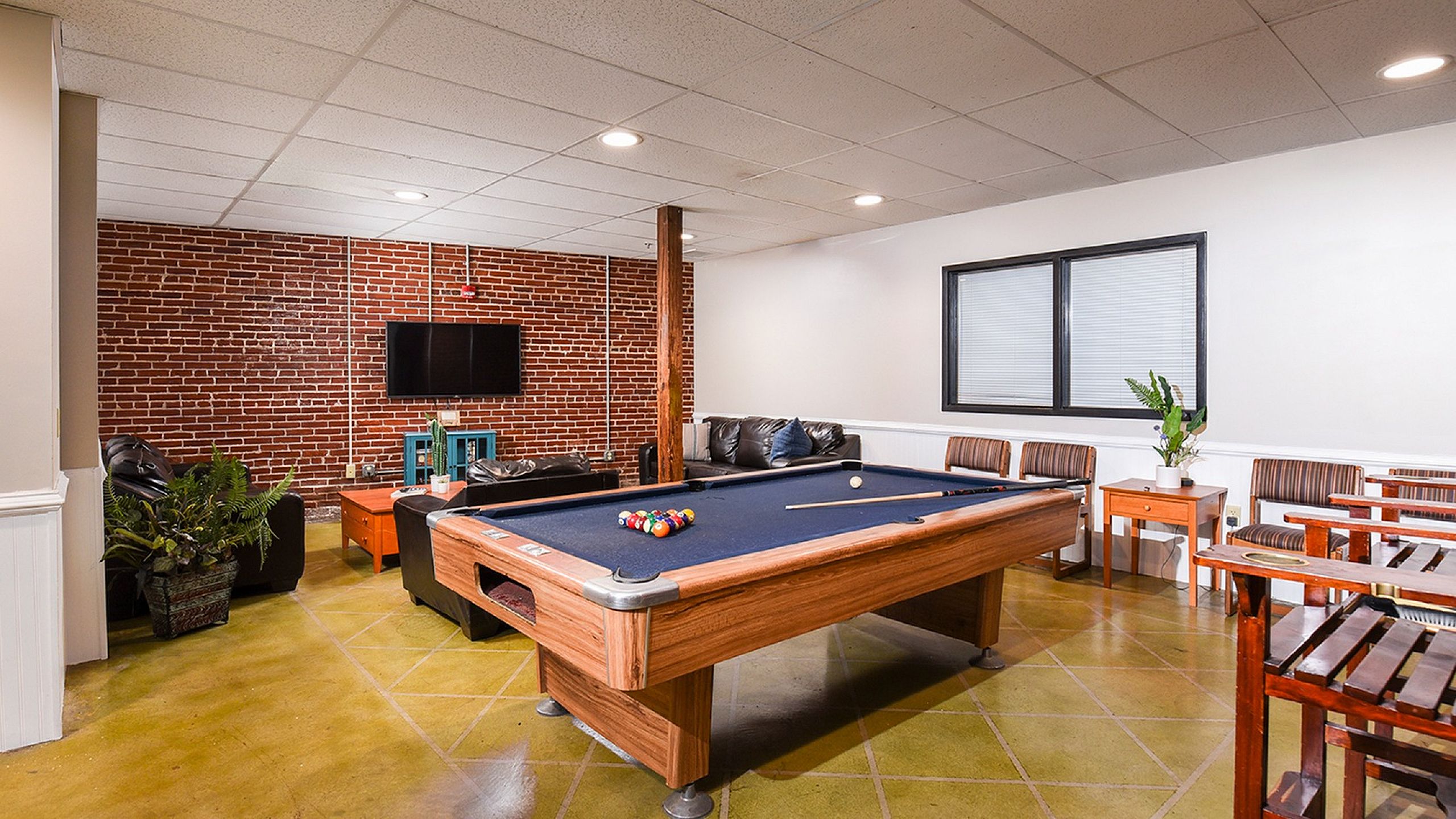 Inviting game room with a modern pool table, cozy seating, and stylish brick accent wall for ultimate relaxation.