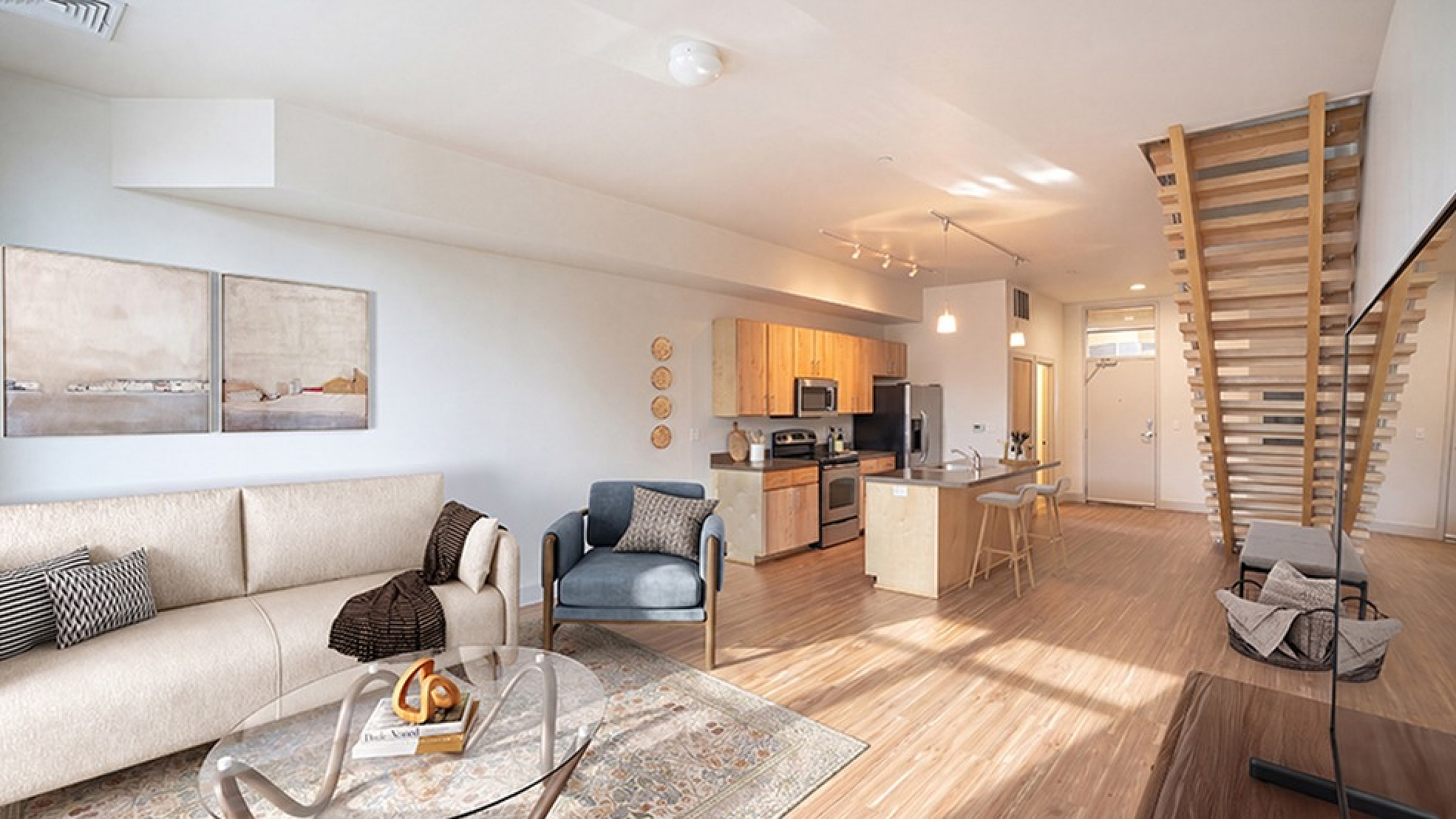 Modern open-concept living room and kitchen with stylish furniture, elegant decor, and wooden staircase in a bright, spacious apartment.