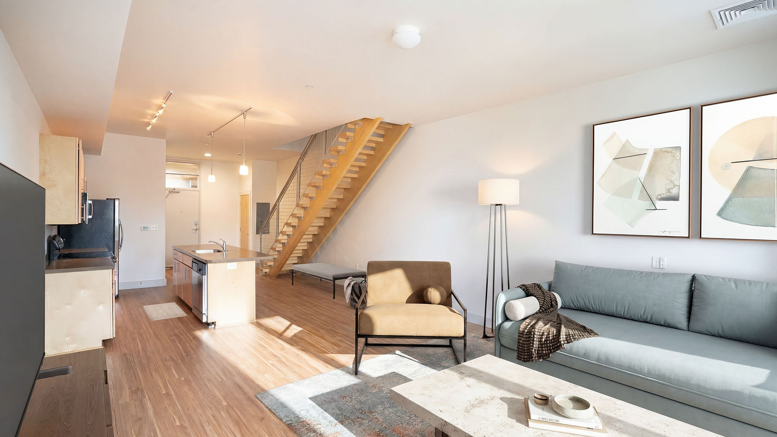 Modern open-concept apartment with stylish kitchen, cozy living room, and inviting wooden staircase.