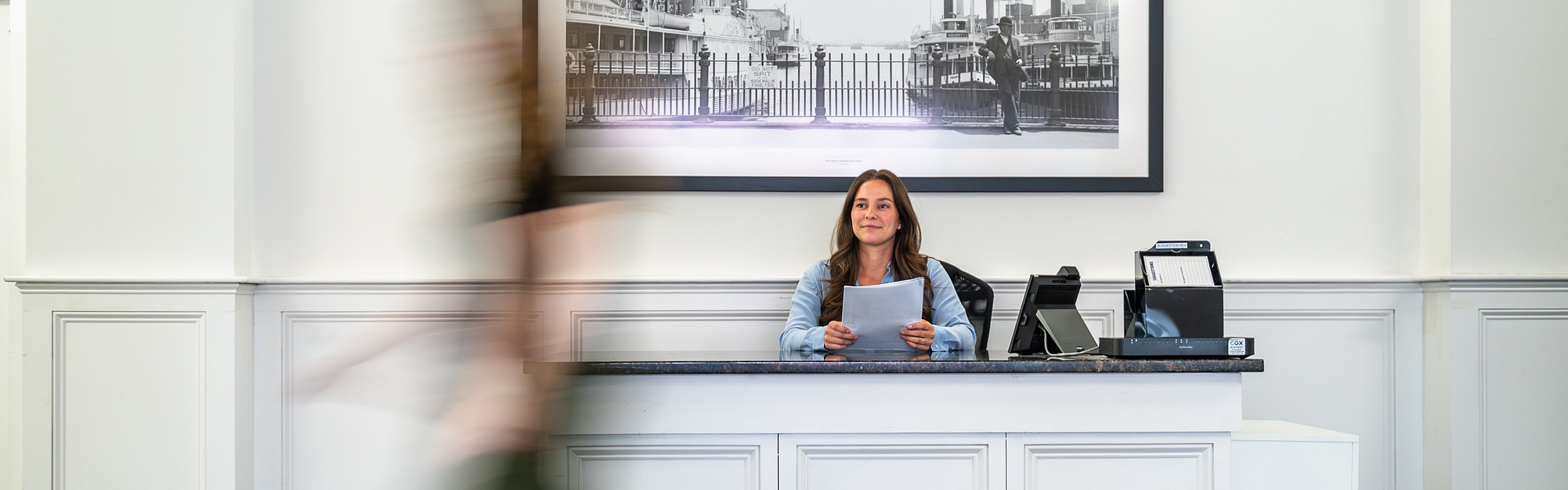 Inviting lobby area with cheerful receptionist at a modern apartment complex, featuring a chic black-and-white cityscape art piece.