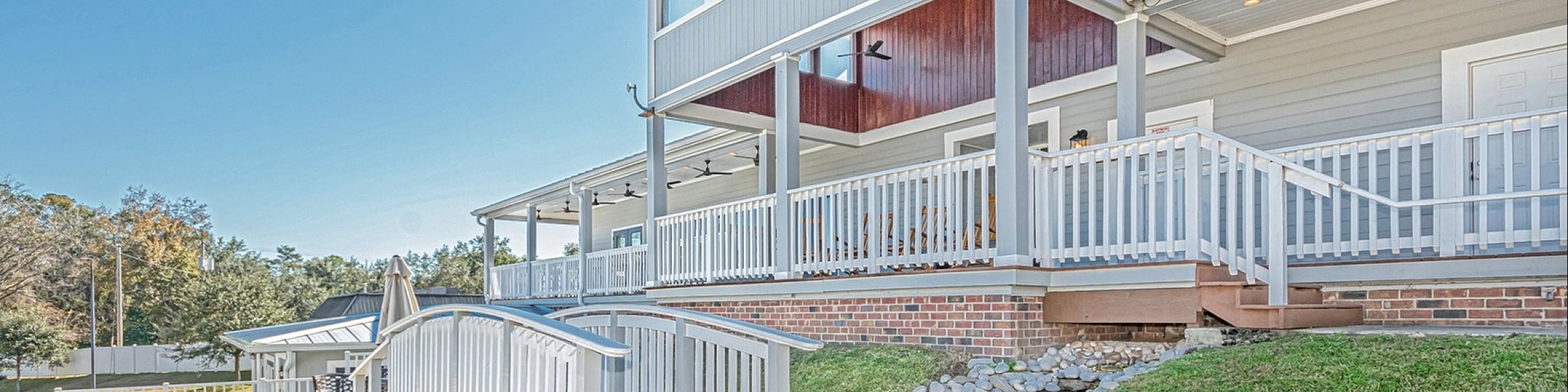 Charming two-story home with expansive wraparound porch, elegant white railing, and a picturesque garden pathway.
