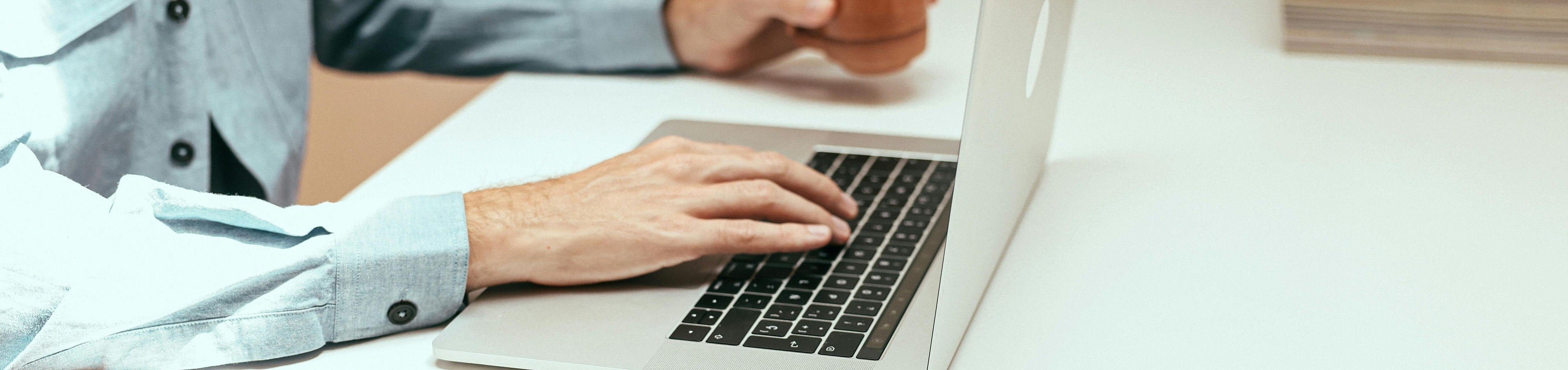 Minimalist workspace with a modern laptop, stylish eyeglasses, and a person enjoying coffee while working.