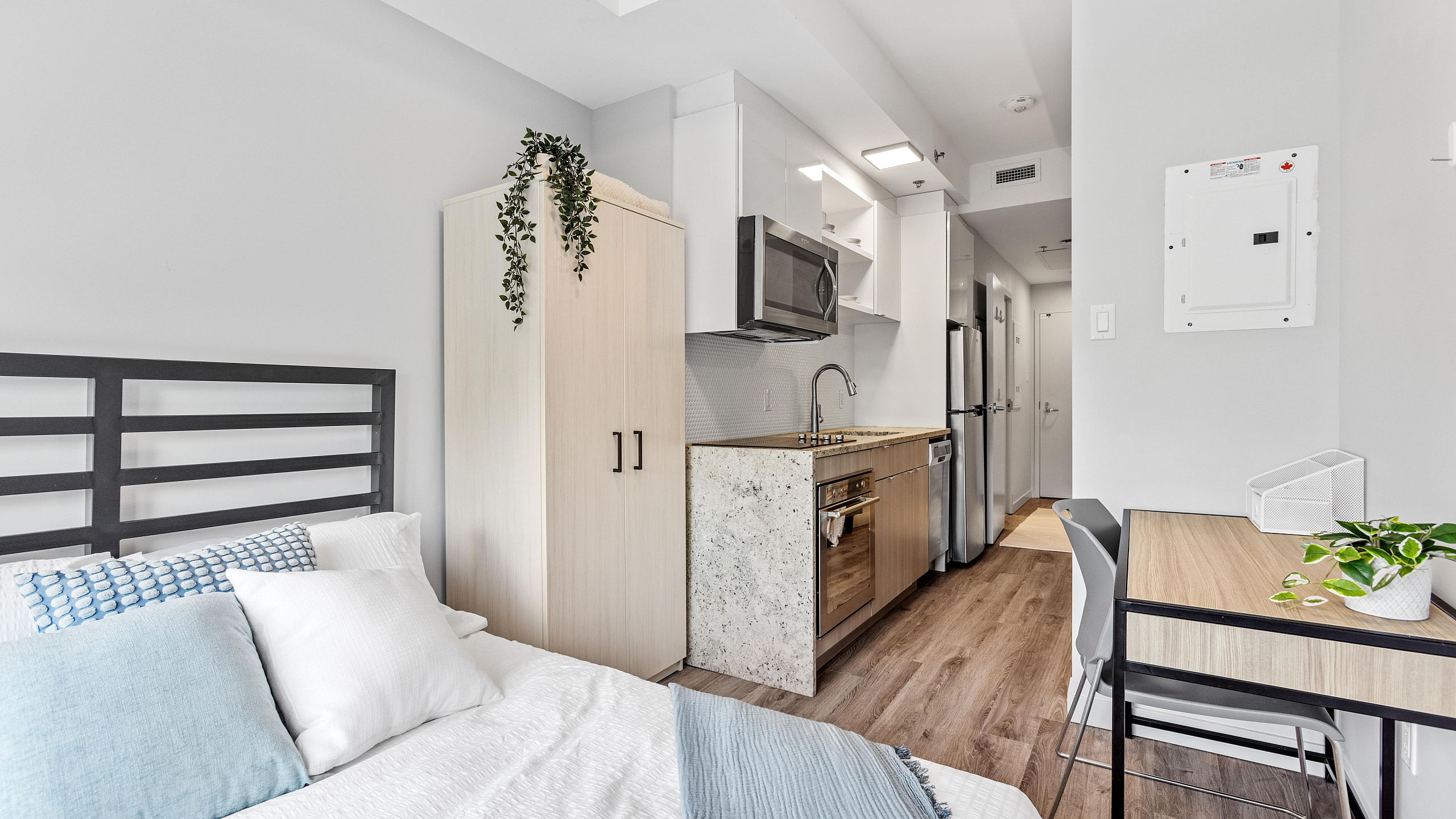 Modern studio apartment with stylish kitchen, cozy bed, and chic workspace, featuring natural light and elegant decor.