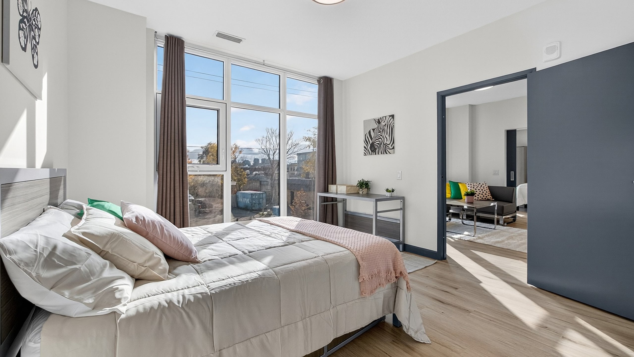 Bright and modern bedroom with large windows, elegant decor, and an inviting atmosphere, opening to a cozy living area.