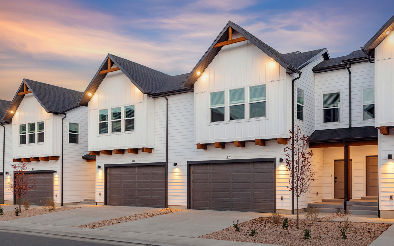 Exterior view of Railrunner townhomes in Roy, Utah, featuring attached two-car garages at dusk.