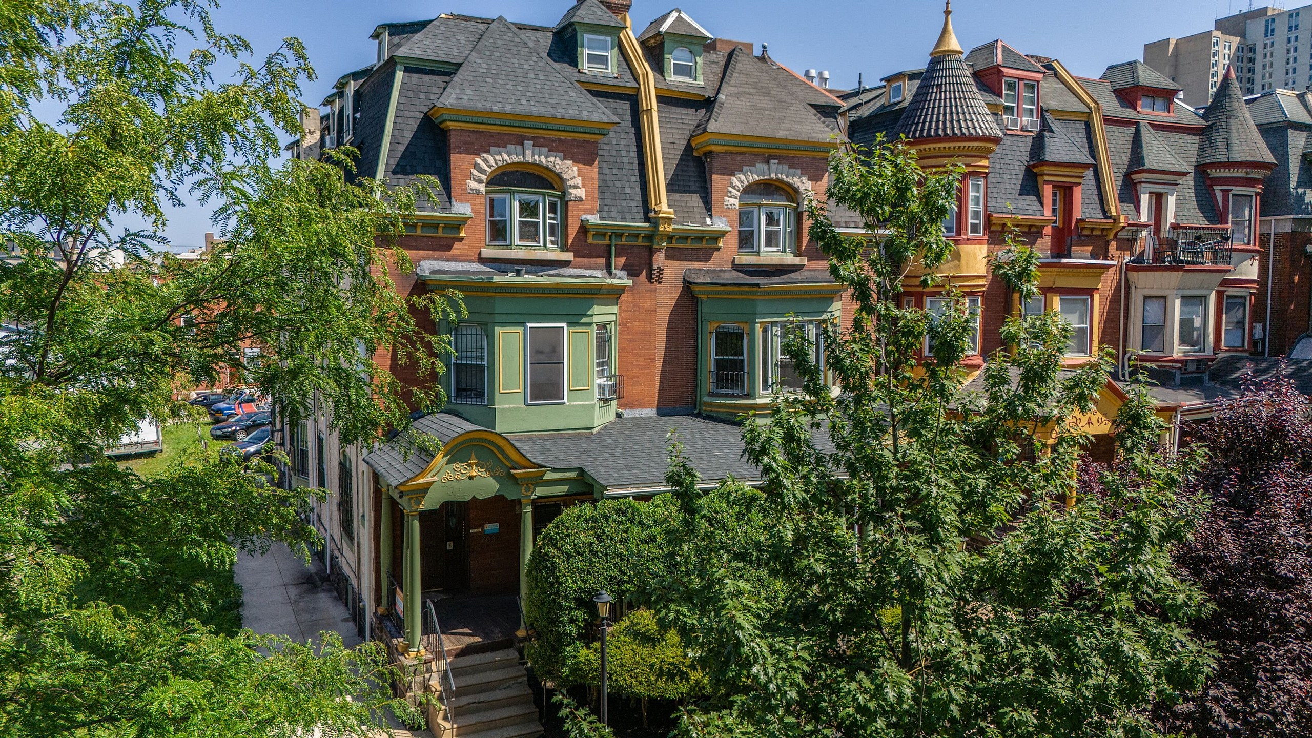 Charming historic apartment building with vibrant red brick facade, ornate detailing, and lush green surroundings in an urban setting.