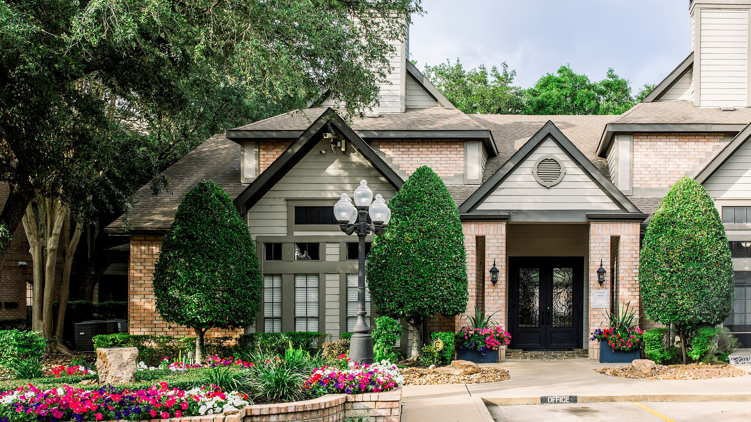 Inviting rustic-style apartment building with lush landscaping, vibrant flowerbeds, and charming brick detailing.