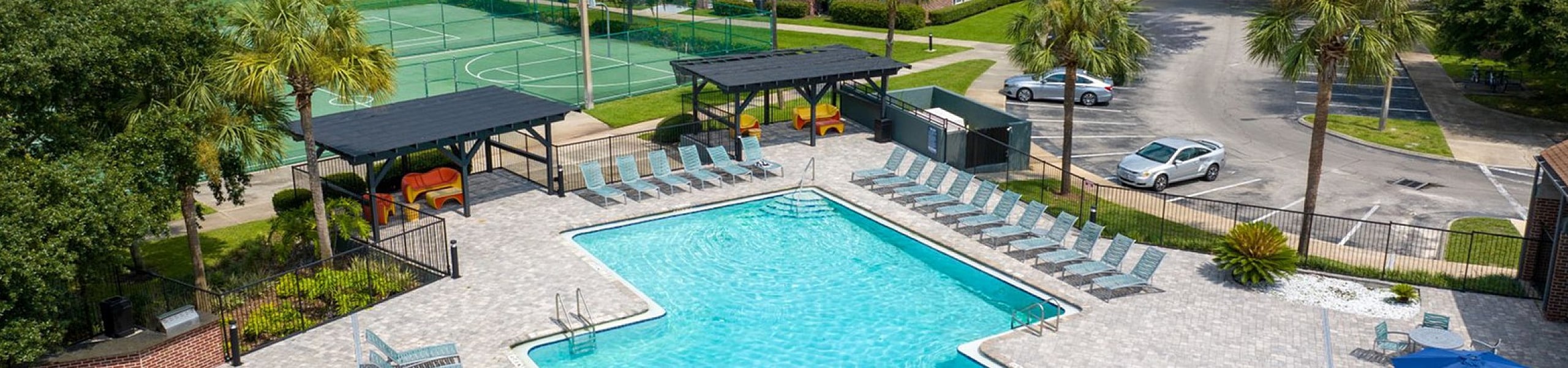 Inviting outdoor pool area with ample lounge chairs surrounded by lush greenery and a tennis court, perfect for relaxation and recreation.