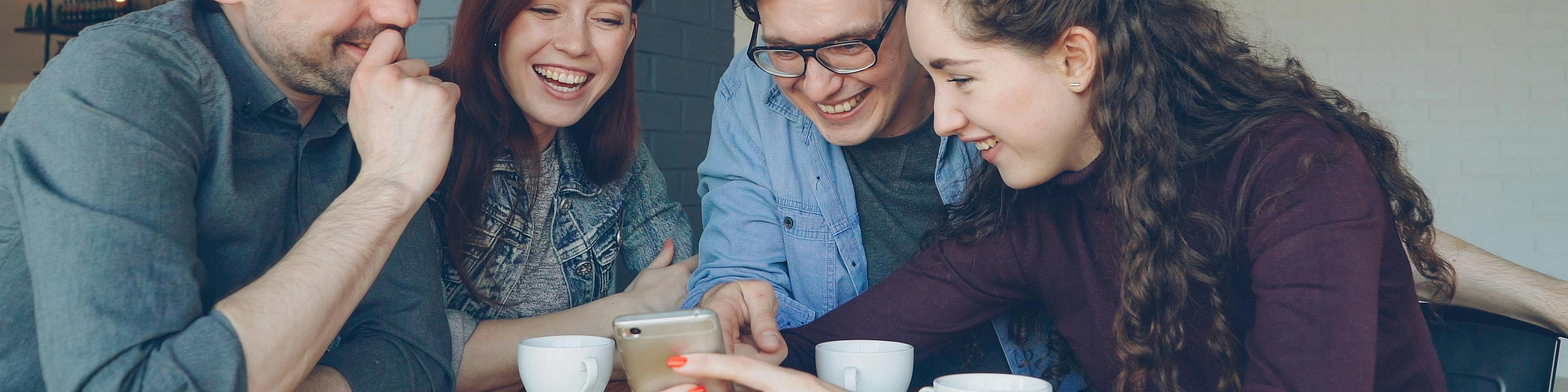 Group of friends sharing a joyful moment over coffee inside a cozy, stylish caf&eacute;.