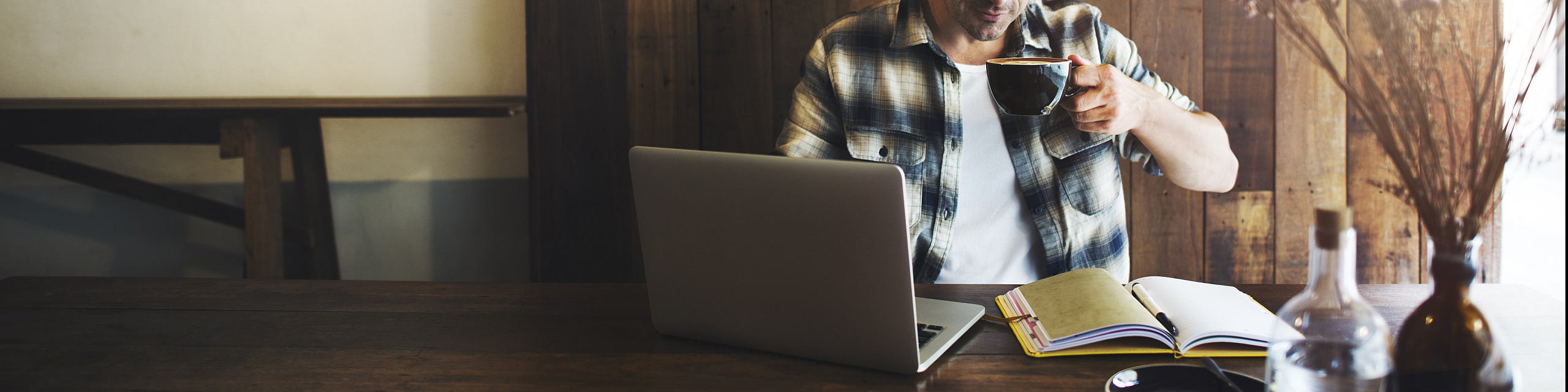 Cozy workspace with a charming rustic vibe, featuring a laptop, open notebook, and a person enjoying coffee.