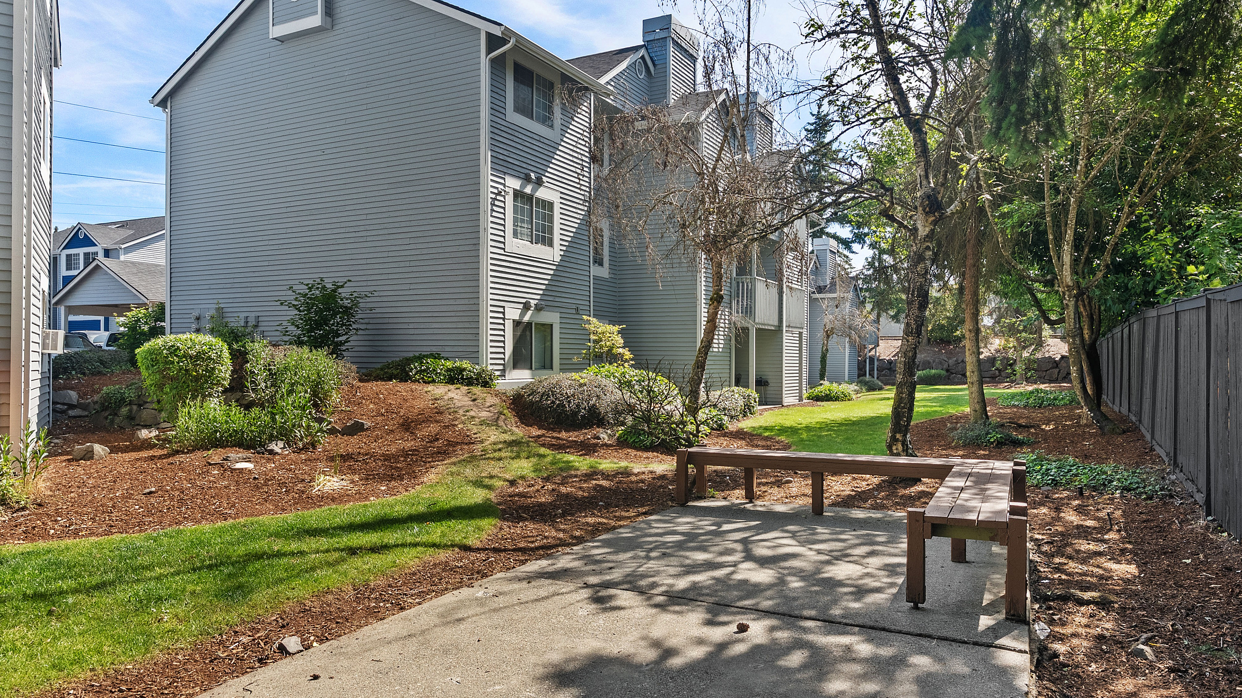 Charming gray apartment building surrounded by lush greenery and a peaceful pathway, perfect for nature lovers seeking tranquility.