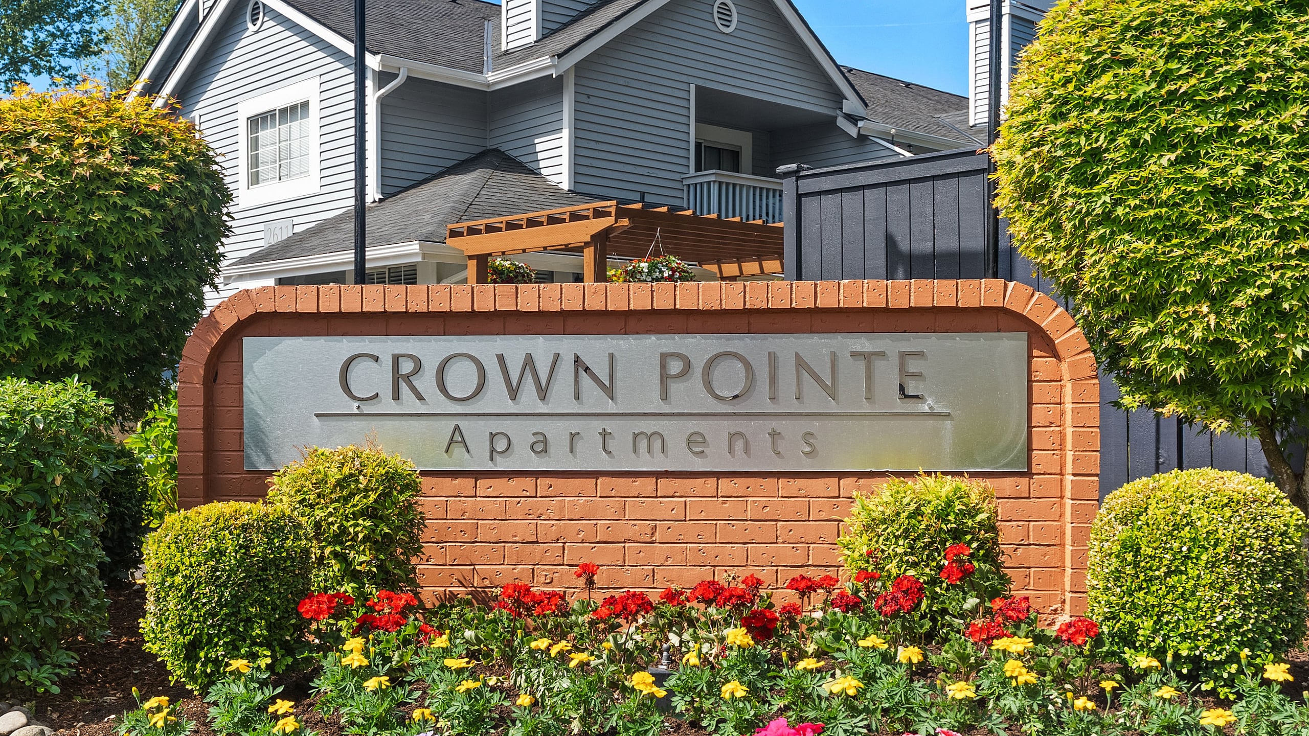 Welcoming Crown Pointe Apartments sign surrounded by vibrant flowers and lush greenery, showcasing inviting architecture in a serene setting.