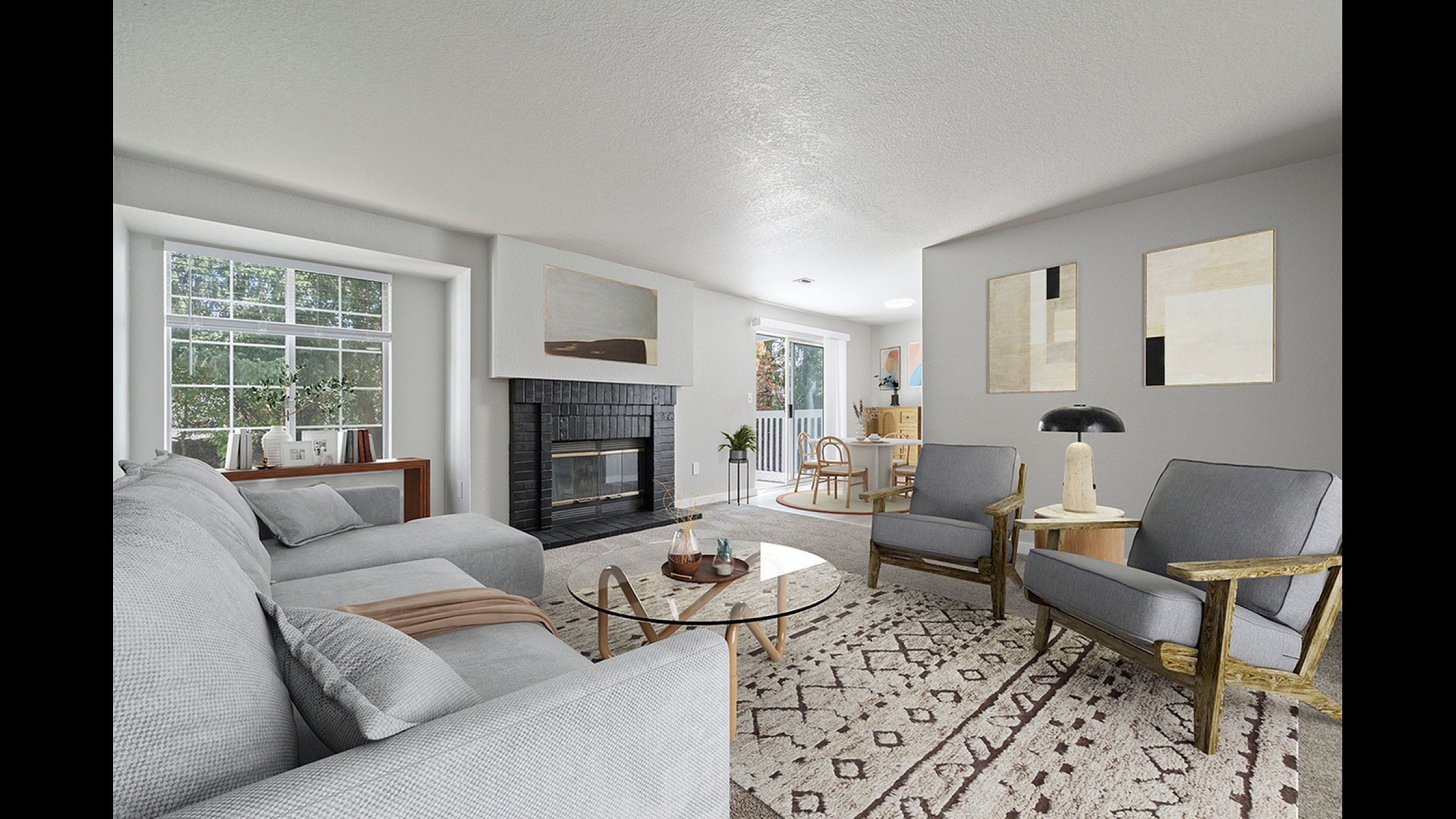 Inviting living room with elegant gray sofa, chic glass coffee table, and cozy fireplace, adjoining a bright dining area with outdoor view.