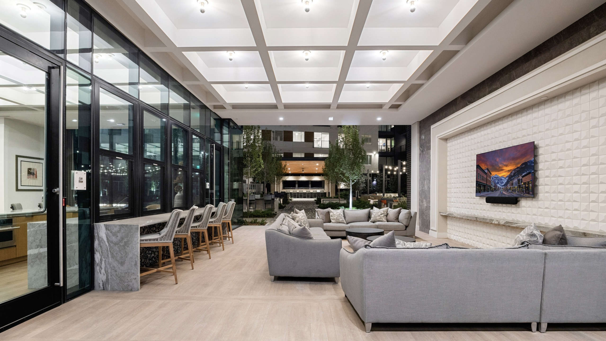 covered outdoor lounge with bar seating and sofas facing a TV and courtyard in background
