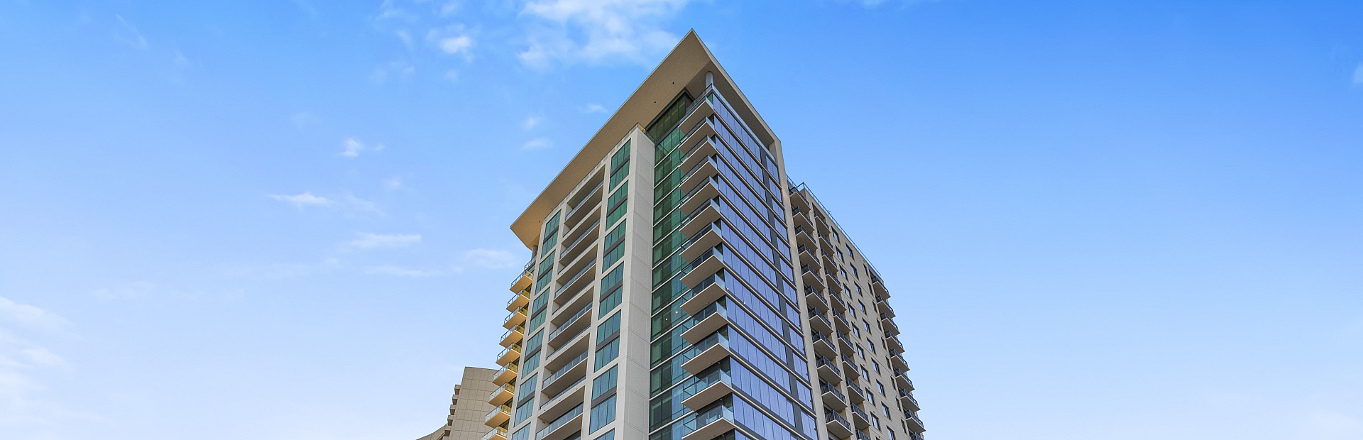 Modern high-rise apartment complex with sleek design and expansive glass windows, surrounded by lush landscaping under a clear blue sky.