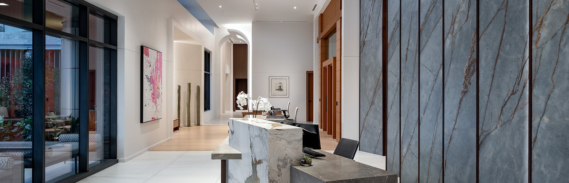 Luxurious modern lobby with sleek marble reception desk, elegant lighting, artistic decor, and floor-to-ceiling windows.